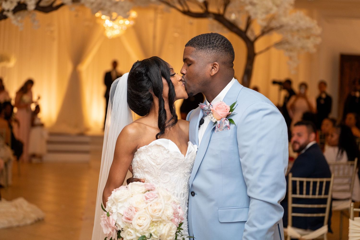 Bride and groom sharing romantic kiss at elegant wedding reception with floral decor.