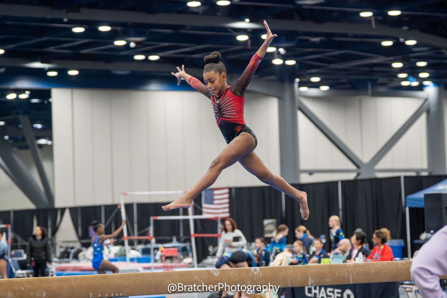 A young gymnast leaps gracefully over the balance beam during a competitive gymnastics meet.