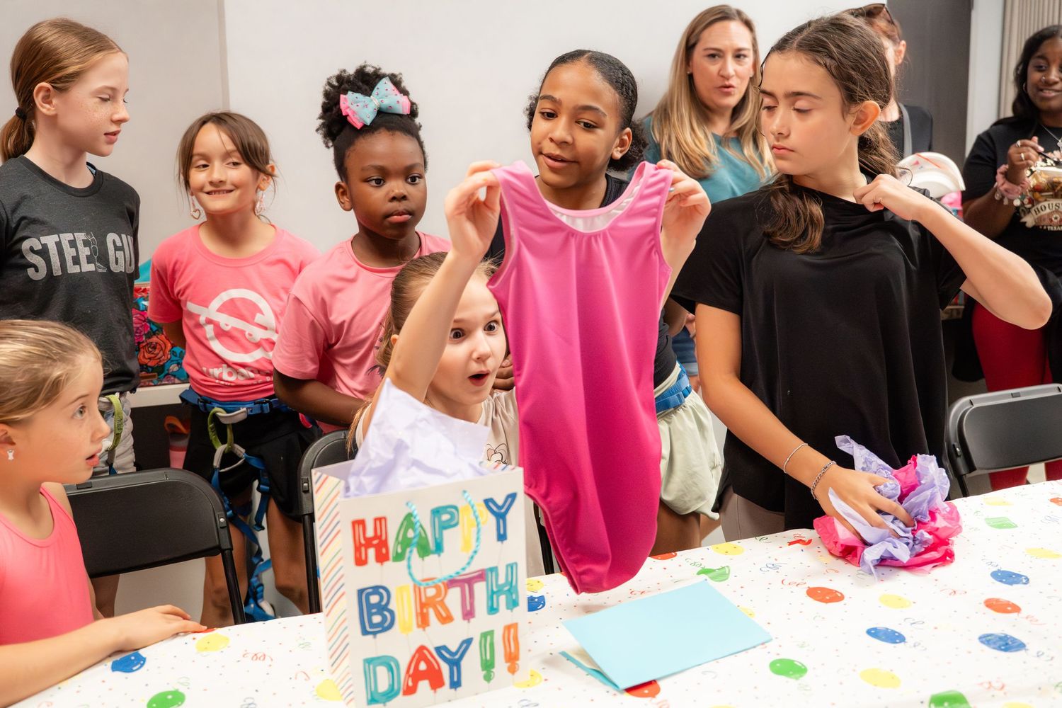 Children gathered around a birthday table opening gifts with a Happy Birthday card.