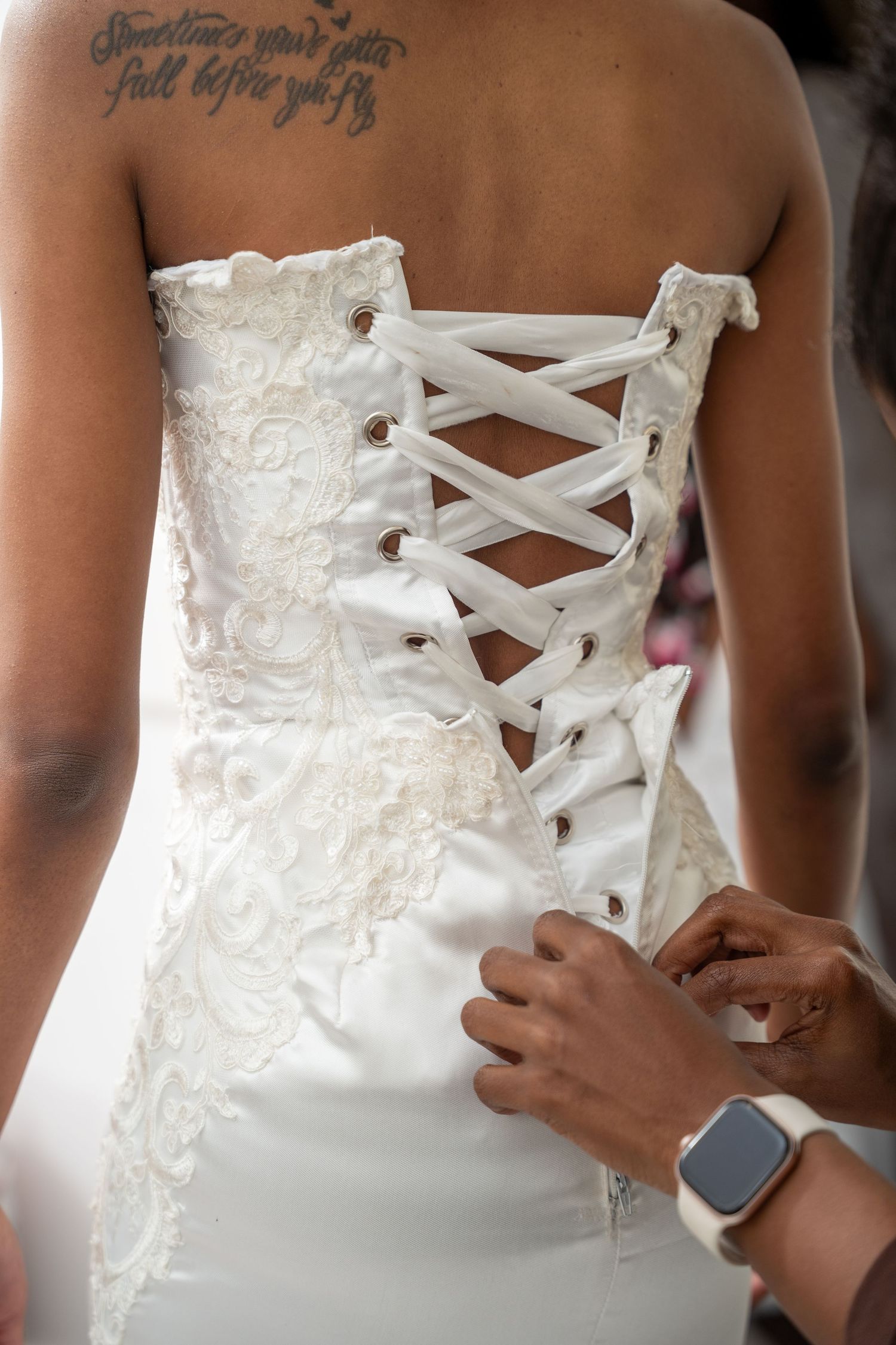 Close-up of bride's white lace corset wedding dress being laced up before ceremony.