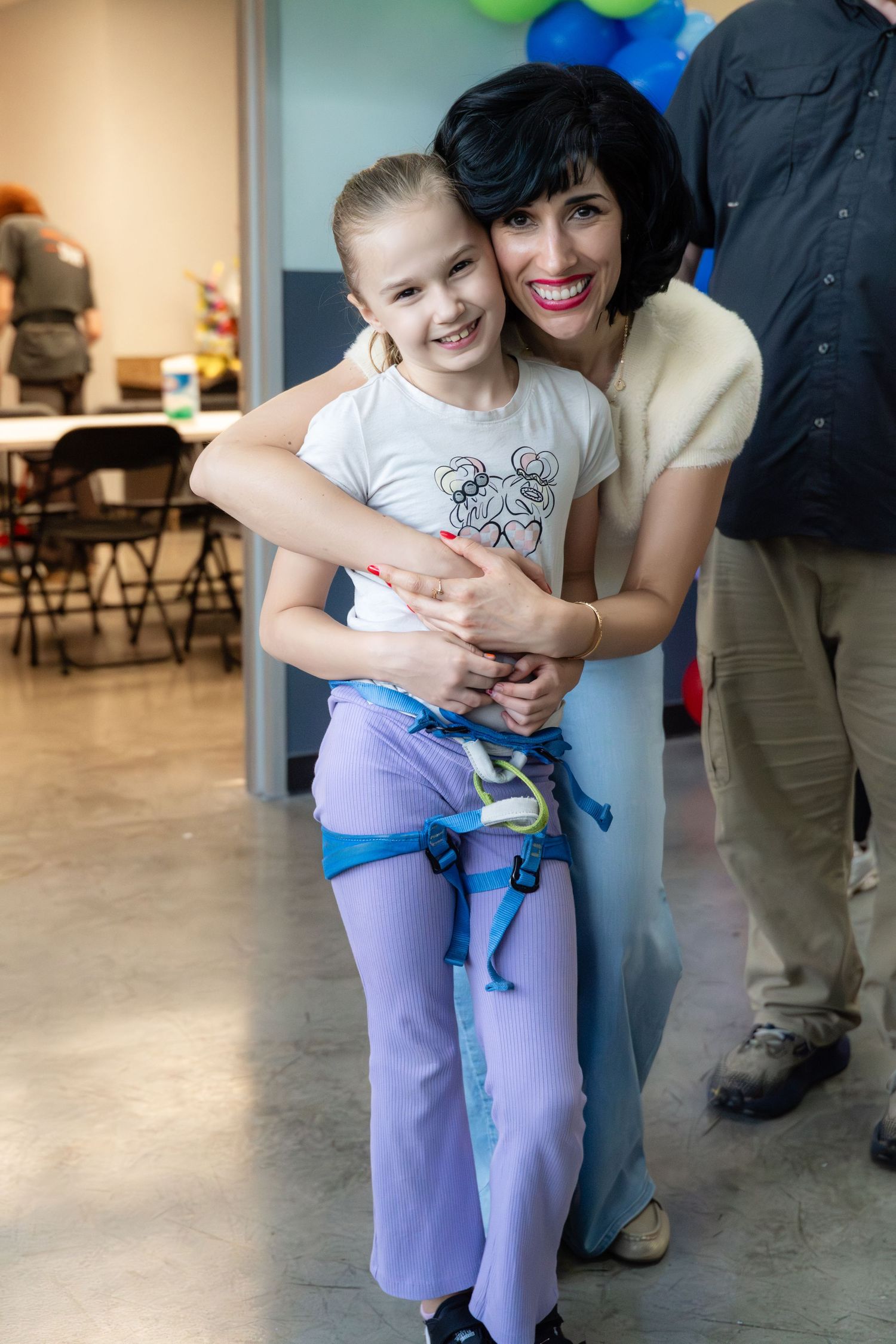 Woman with dark hair hugging and smiling with a young girl at a birthday party.
