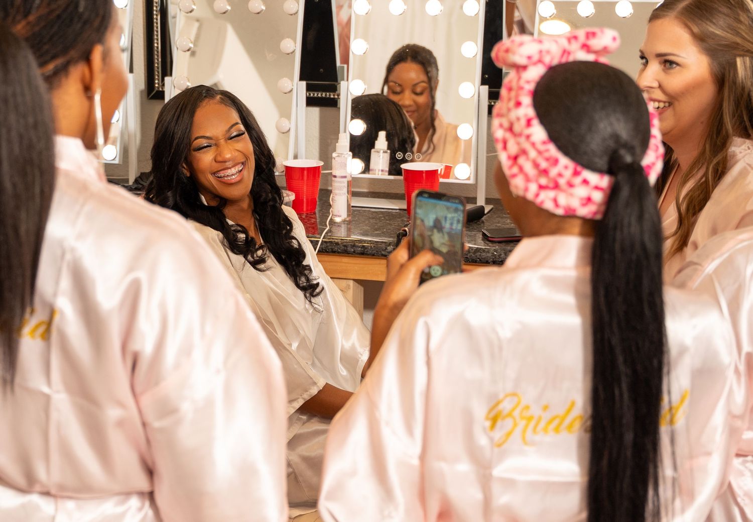 Bride and bridesmaids in satin robes laughing together during pre-wedding getting ready session.