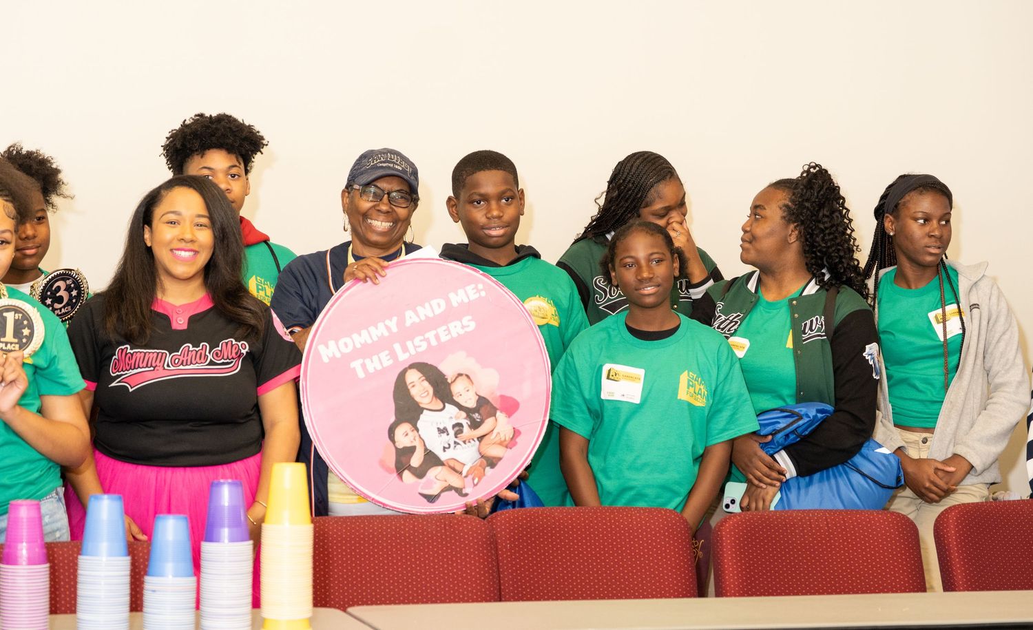 Group of youth program participants pose together holding a decorative heart sign at an event.