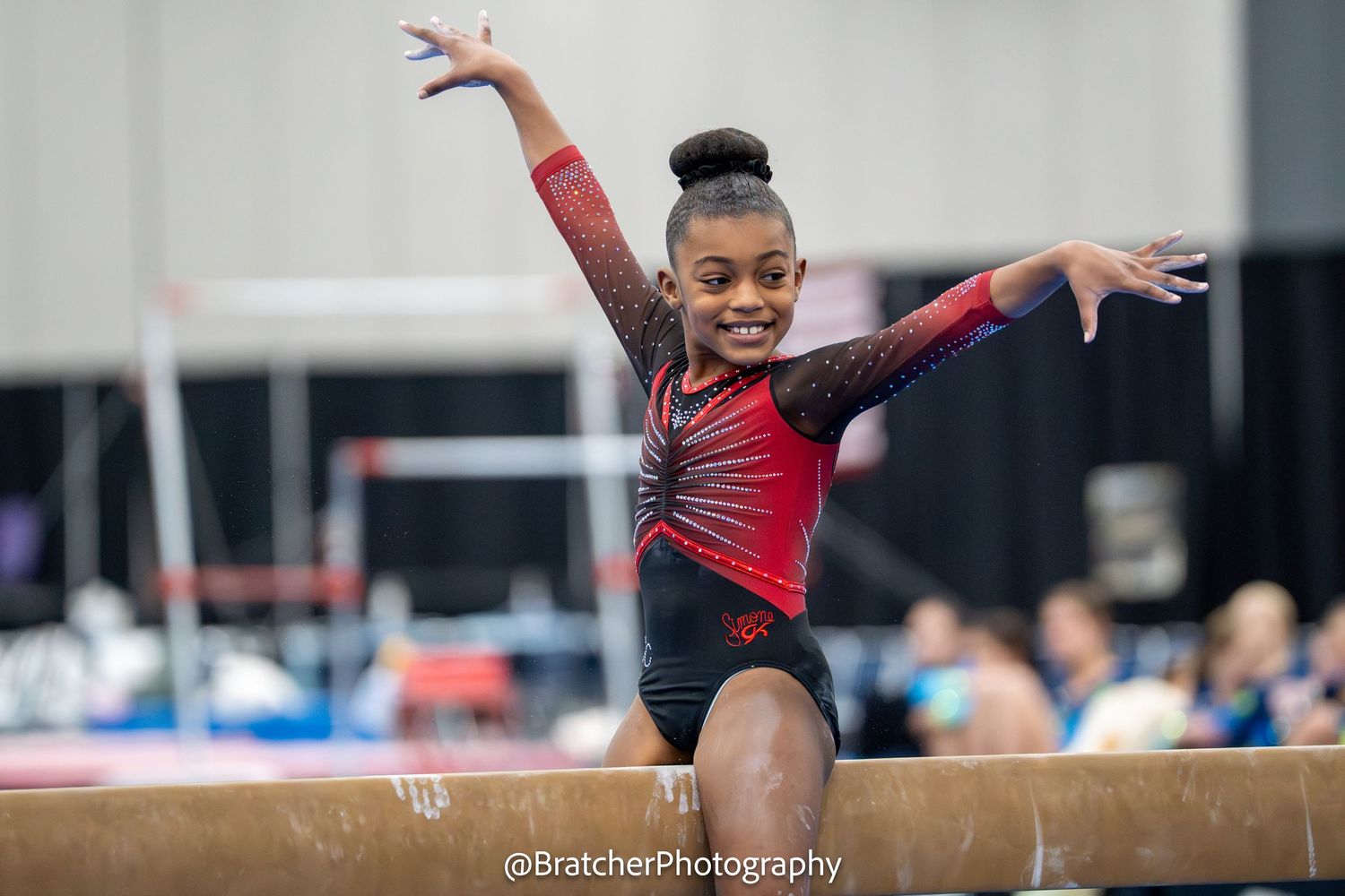 Smiling young Black gymnast balances on beam in sparkly red leotard at gymnastics competition. bratcher photography and houston photographer