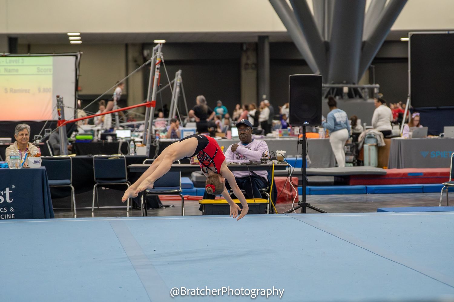 Gymnast performs dynamic back walkover on floor exercise at competitive gymnastics tournament indoors.