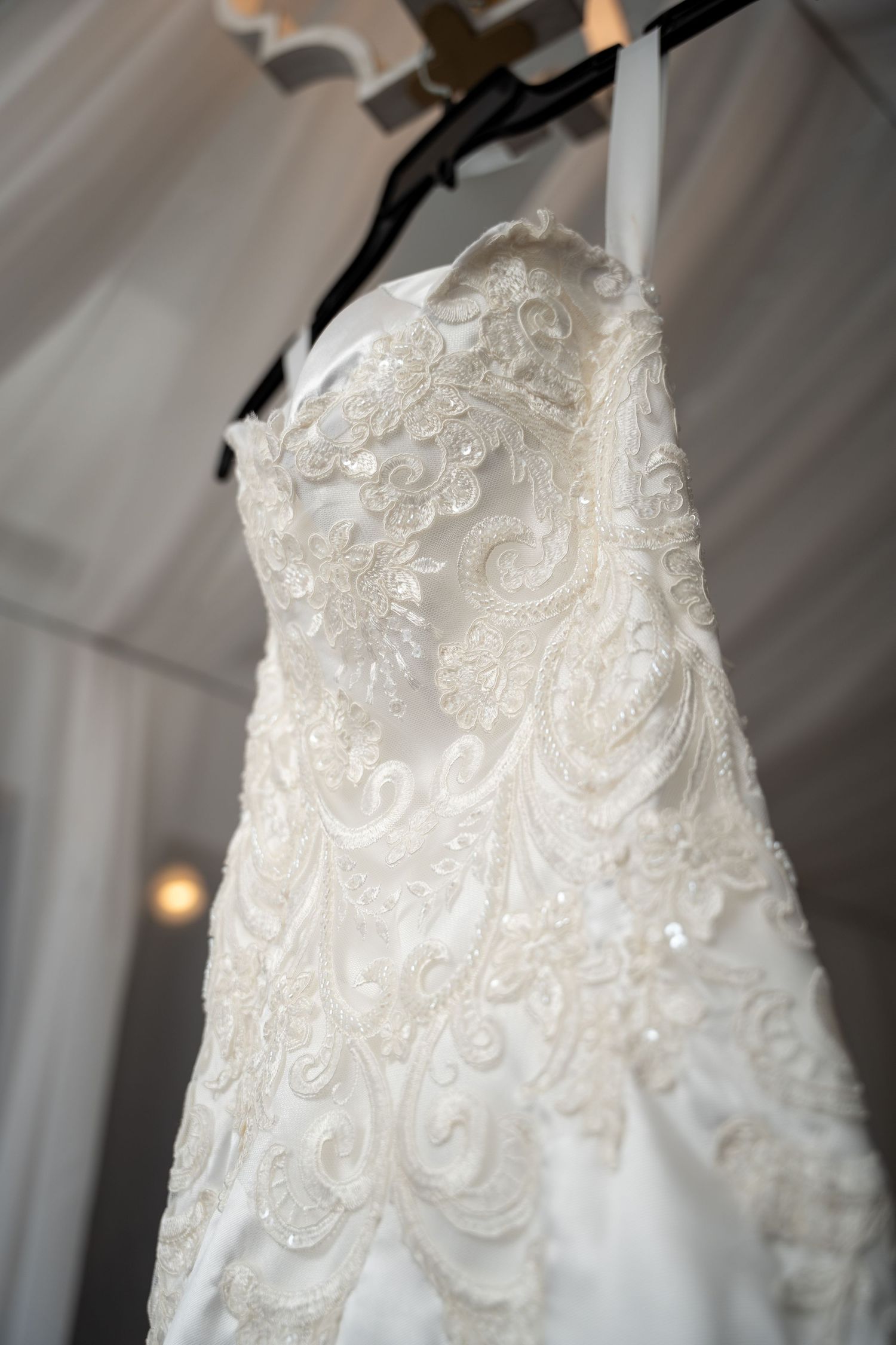 Elegant white strapless lace and beaded wedding gown hanging on display before ceremony.