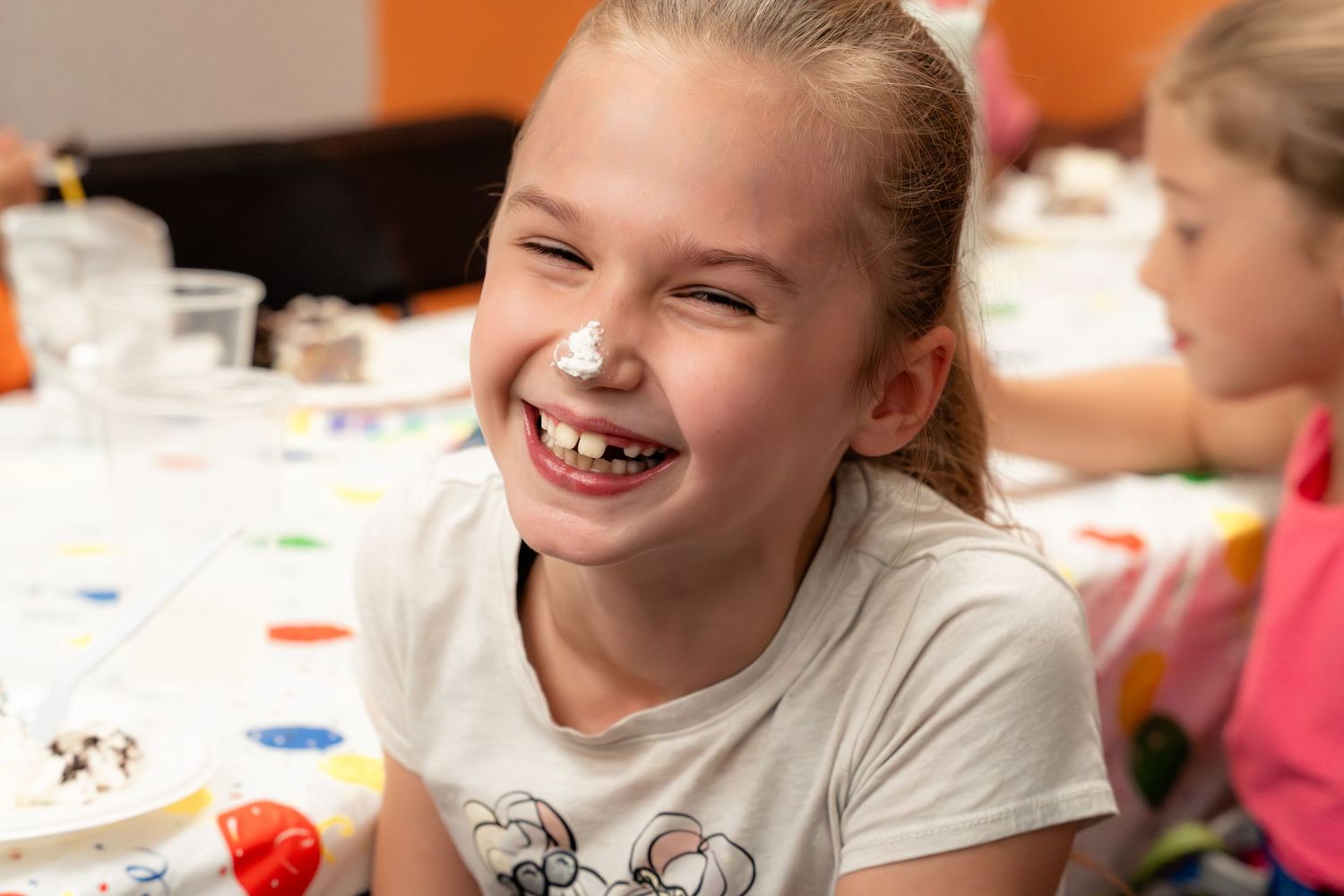 Laughing girl with frosting on her nose enjoying a birthday party celebration.
