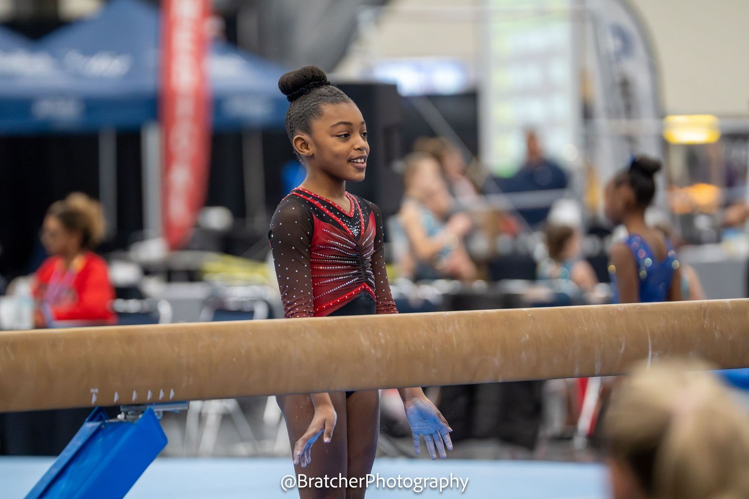 A young female gymnast stands confidently on the balance beam at a gymnastics competition.