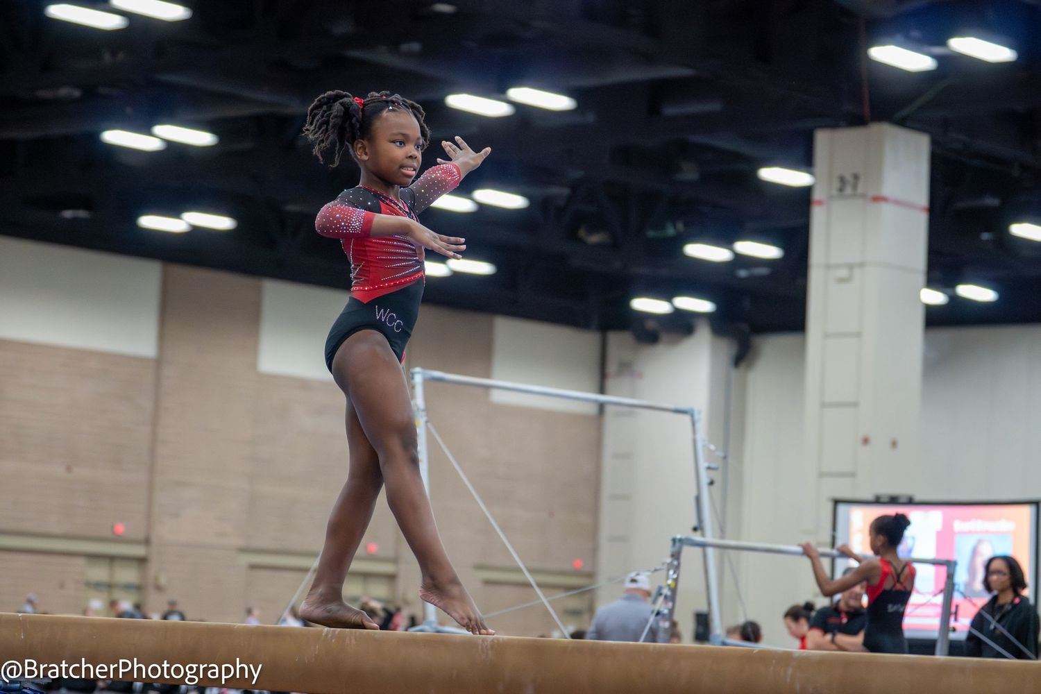 Young gymnast performing a balance beam routine at an indoor gymnastics competition.