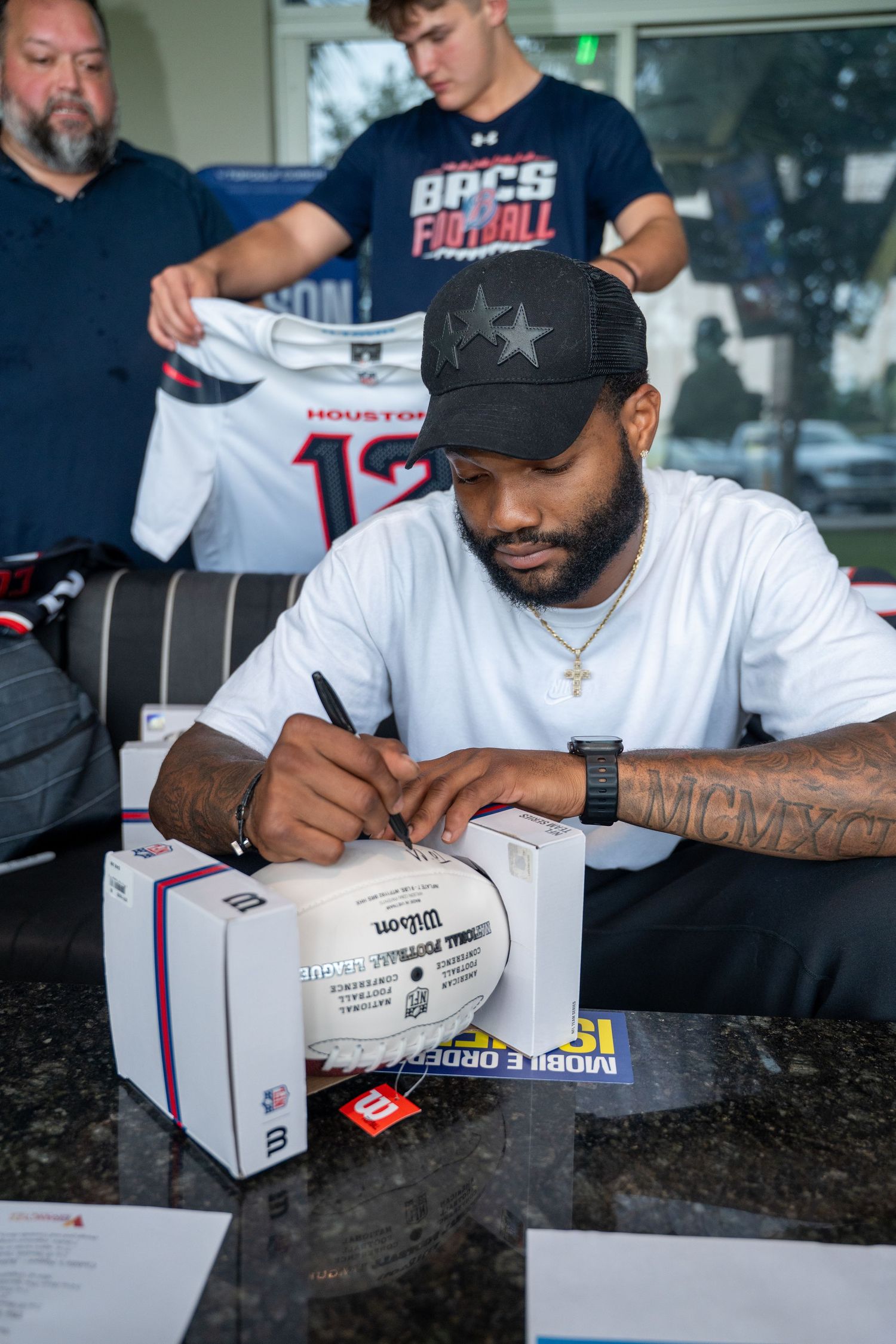 Houston Texans football player signing autographs at a fan event table.