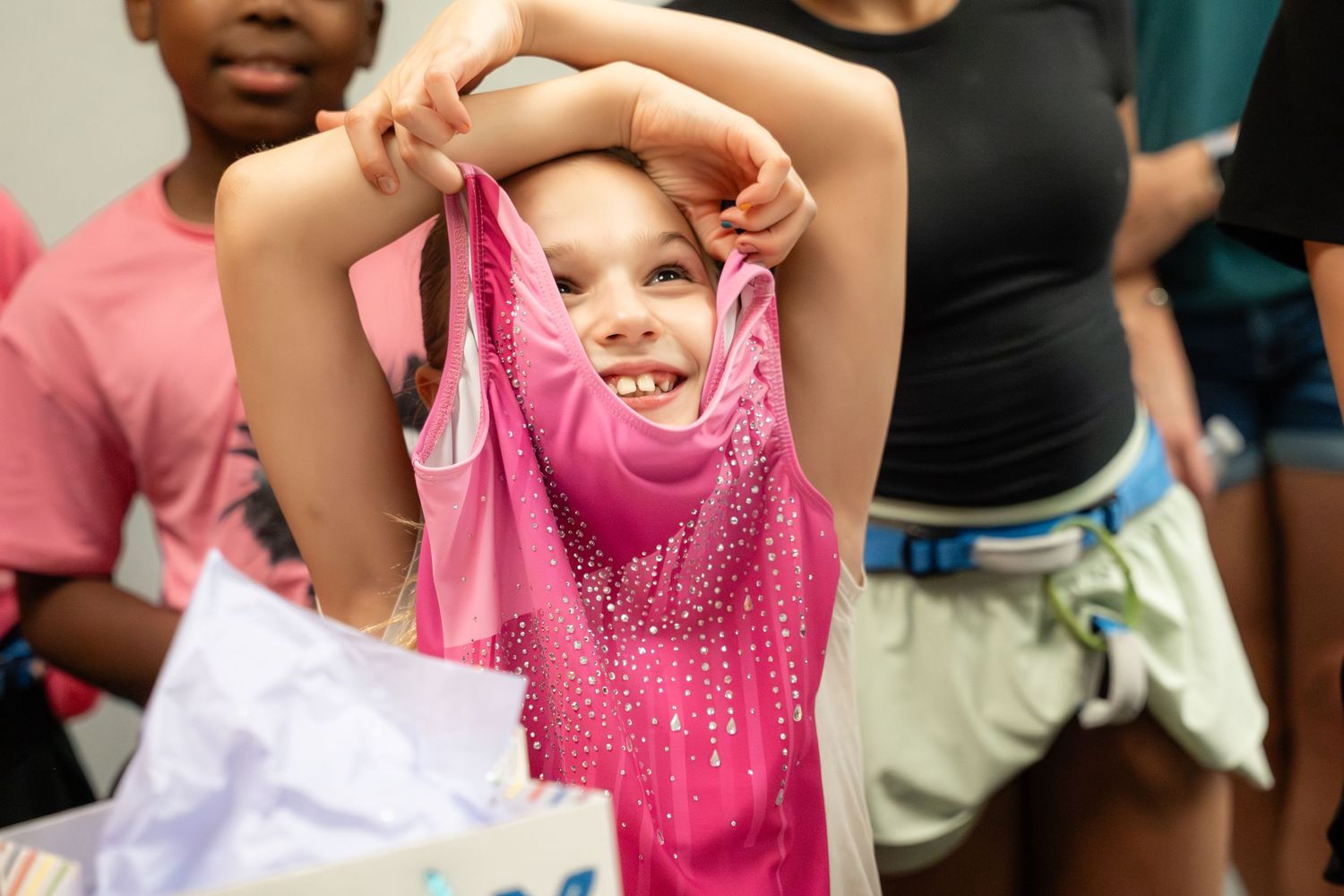 Young girl smiling while holding up a pink sparkly gymnastics leotard at a birthday party.