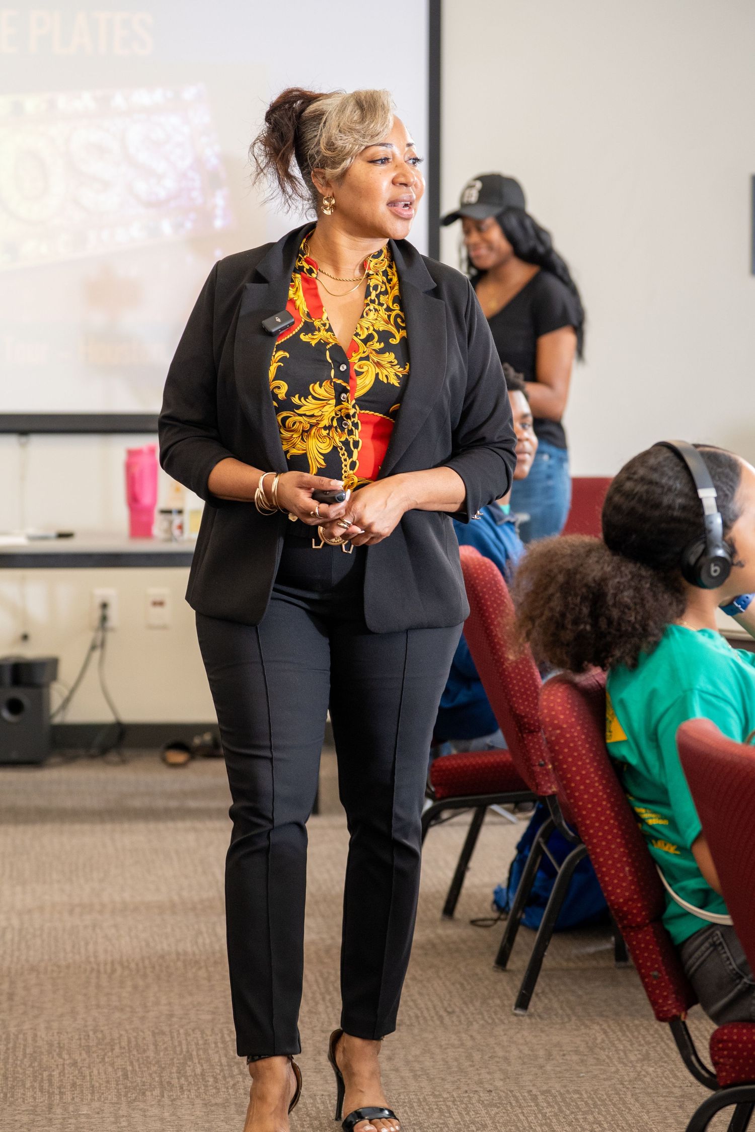 Black woman in black blazer and floral top presenting to audience in conference room setting. bratcher photography and houston photographer
