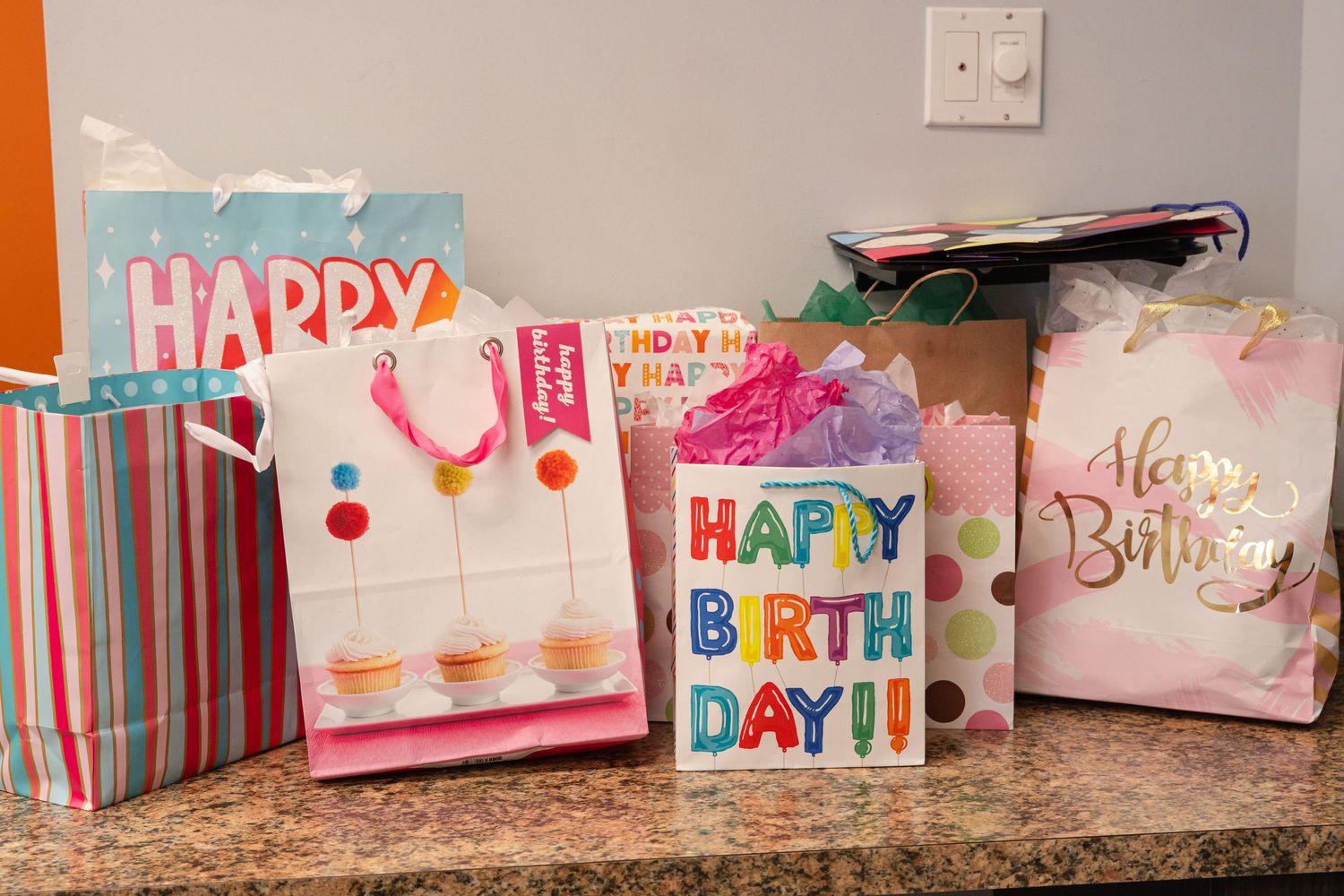 Four colorful Happy Birthday gift bags arranged on a counter for a celebration.