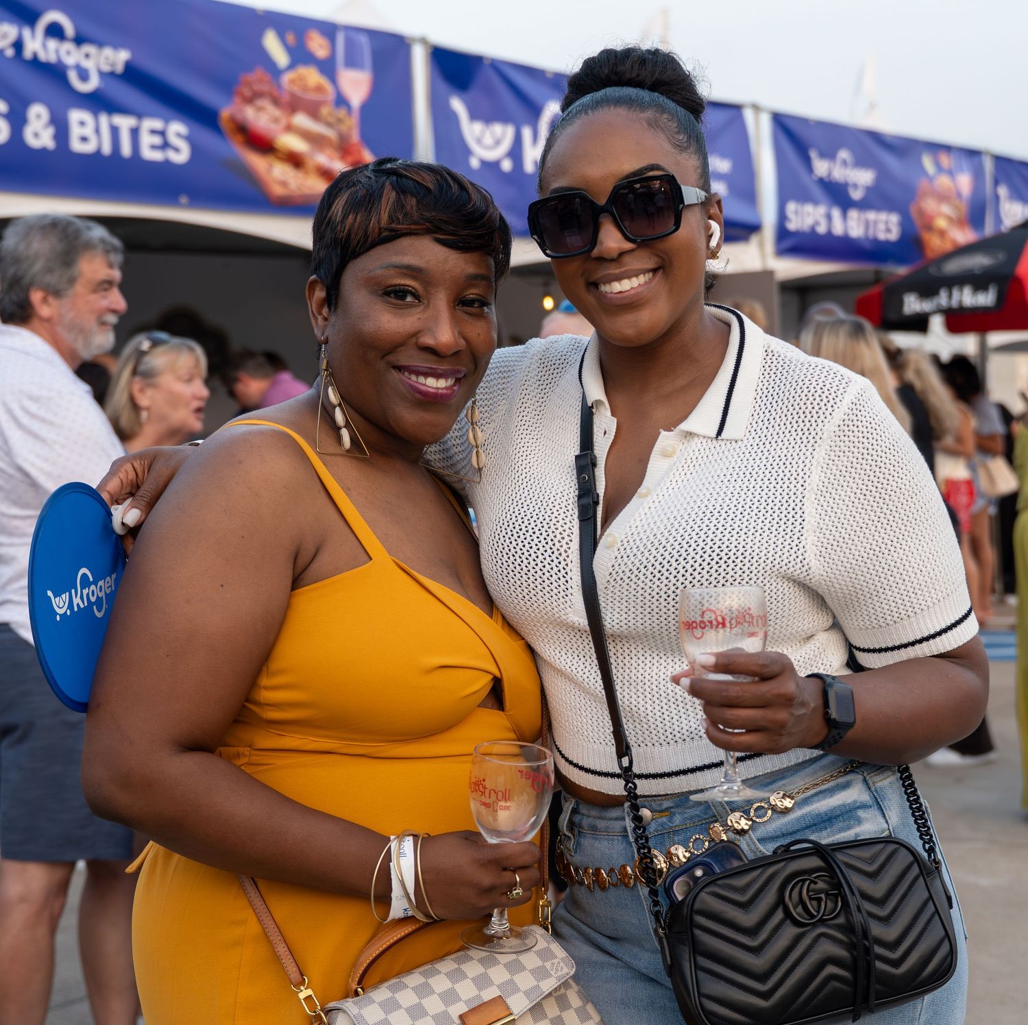 Two women smiling and holding drinks at an outdoor Kroger Sips and Bites event.