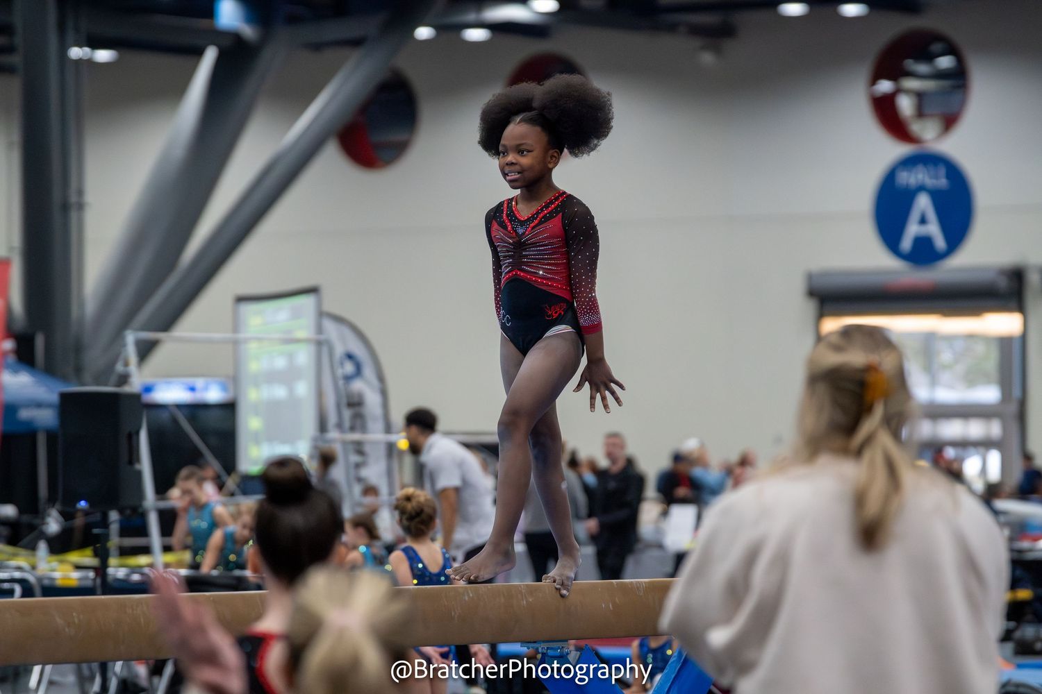 Young gymnast performs balance beam routine at indoor gymnastics competition. bratcher photography and houston photographer