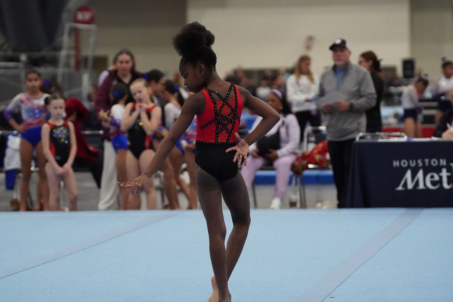 Young female gymnast stands on floor exercise mat during gymnastics competition. bratcher photography and houston photographer