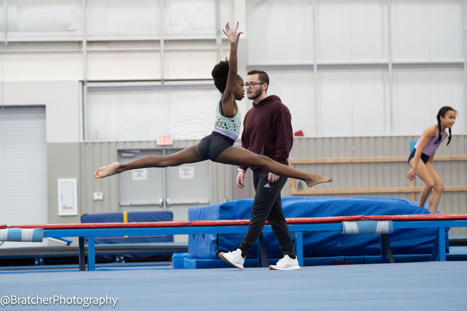 Female gymnast practices split leap on balance beam with coach spotting during gymnastics training session. bratcher photography and houston