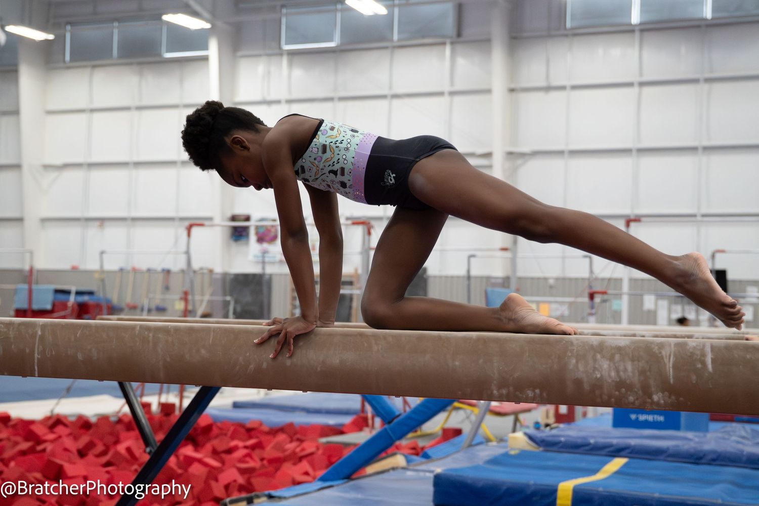 Female gymnast holds prone balance position on gymnastics beam during practice or competition. bratcher photography and houston photographer
