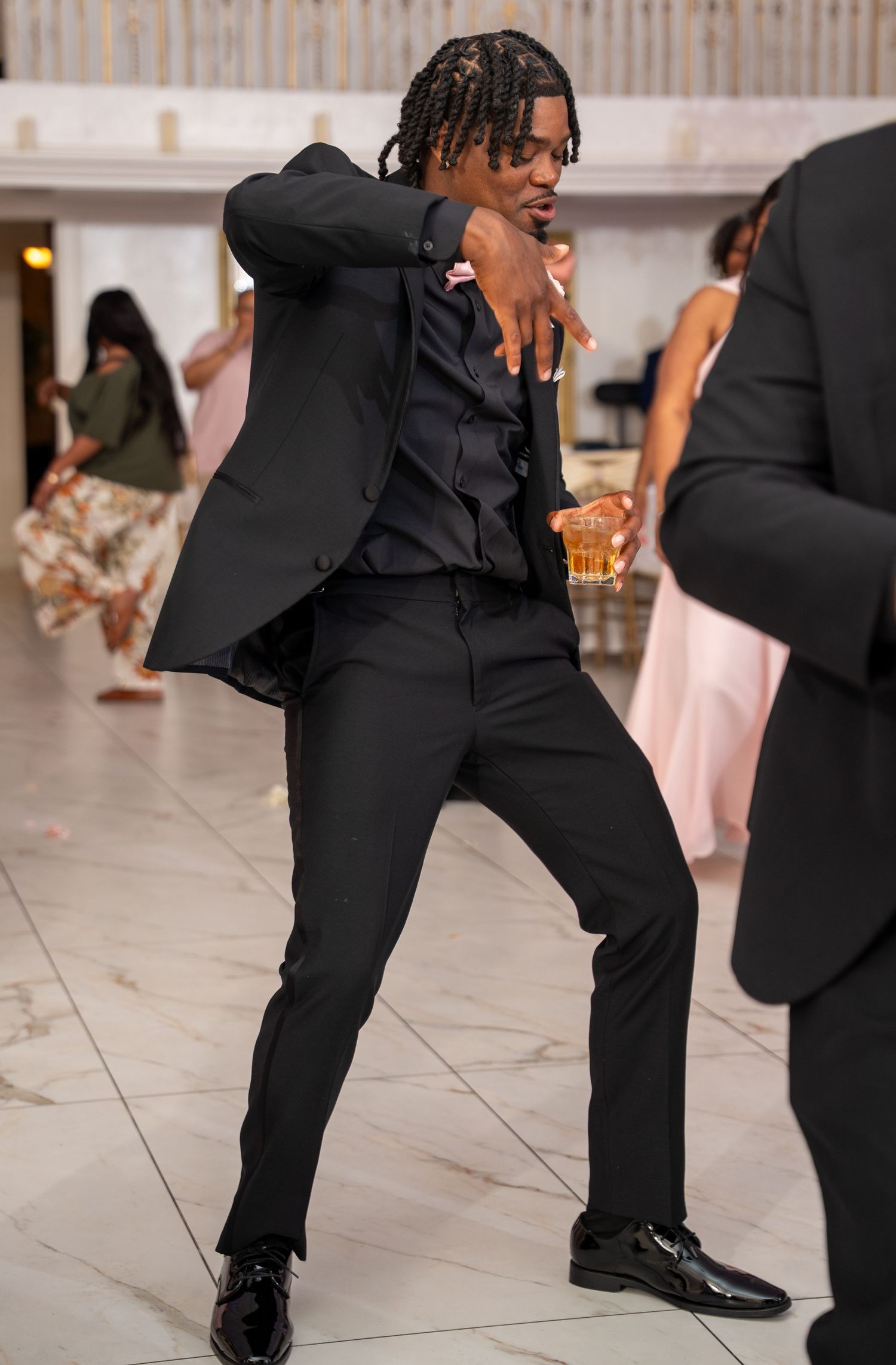 Guest in black suit energetically dancing at wedding reception on marble dance floor.