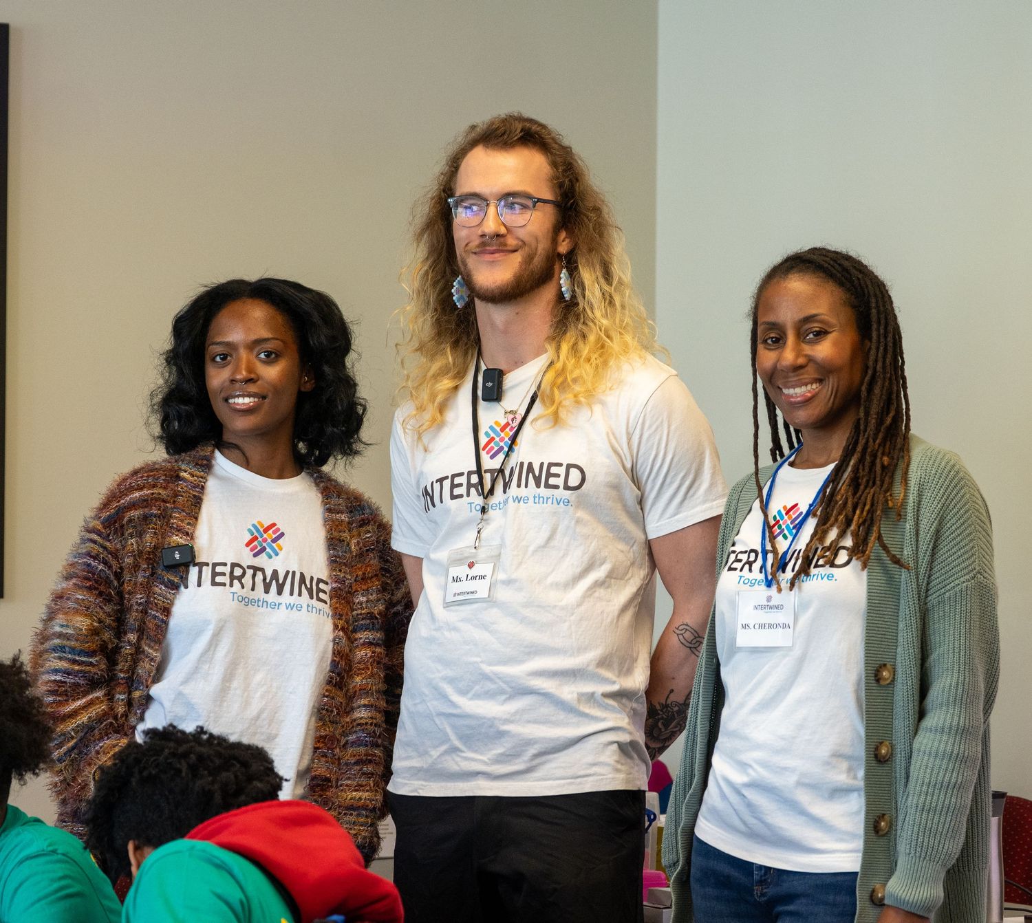 Three smiling volunteers wearing Intertwined white t-shirts pose together at a community event.
