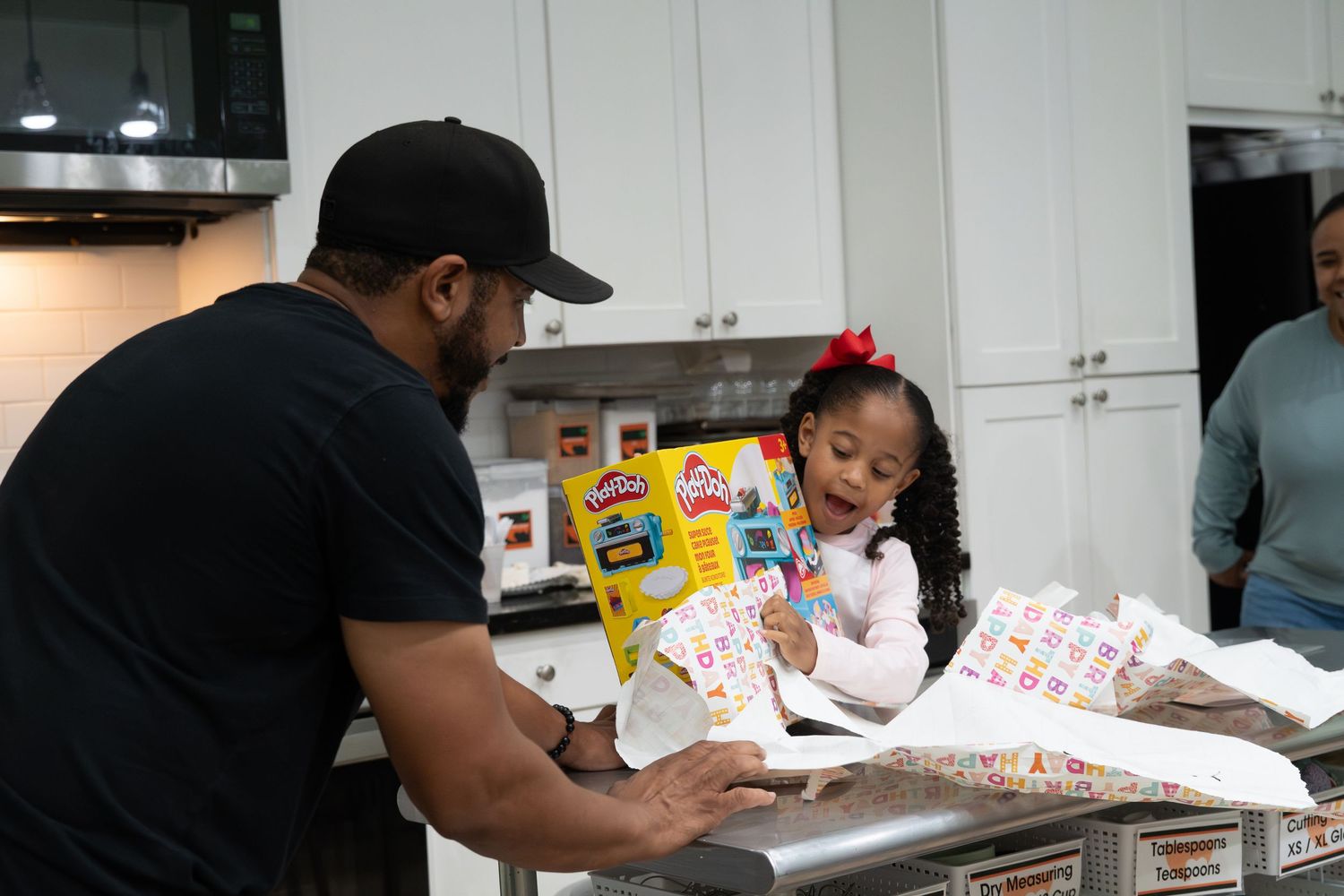 Man shows a young girl birthday stickers and decorations at a kitchen counter celebration.