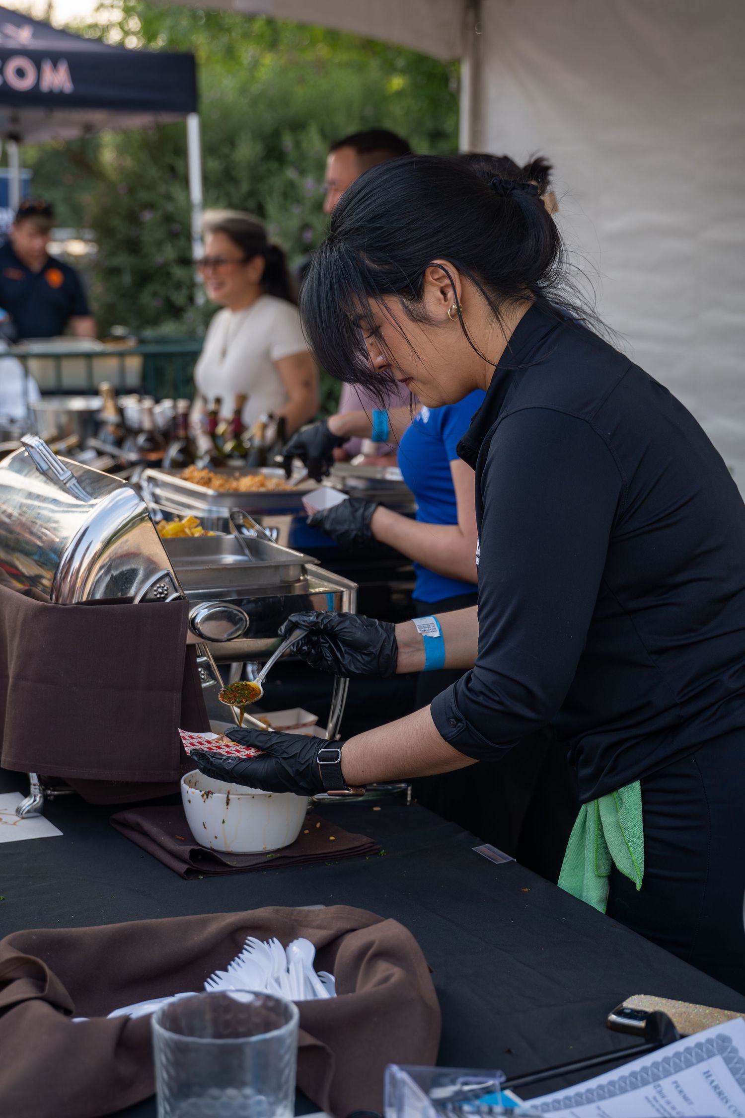 Catering staff member in black uniform serving food at an outdoor event buffet table.