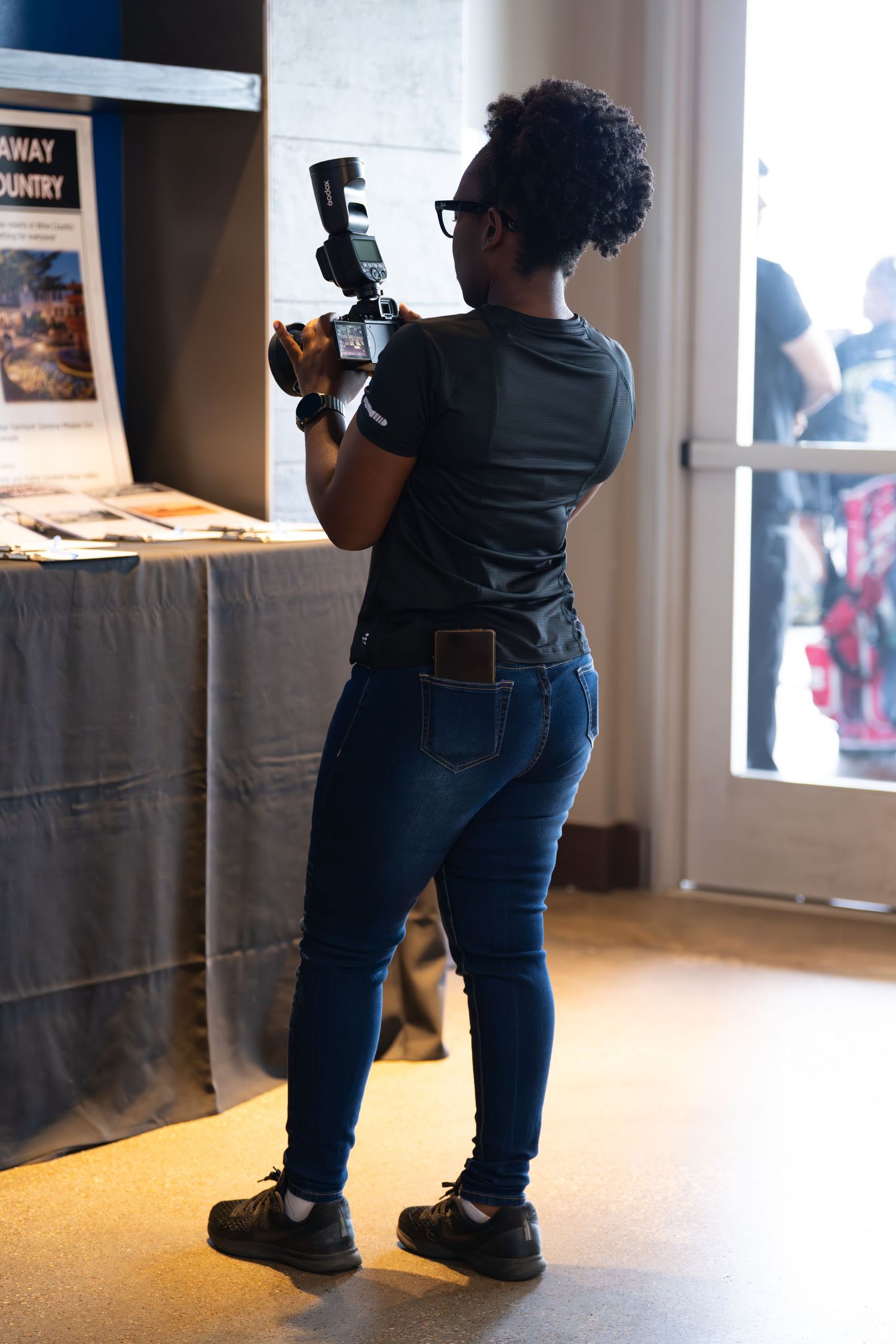 Black woman photographer holding camera with flash, photographing artwork at indoor exhibition event. bratcher photography and houston