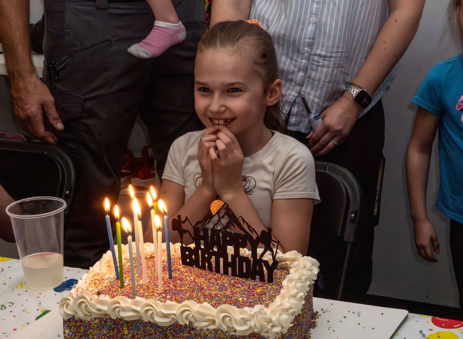 Young girl making a wish over a lit birthday cake with Happy Birthday candles.