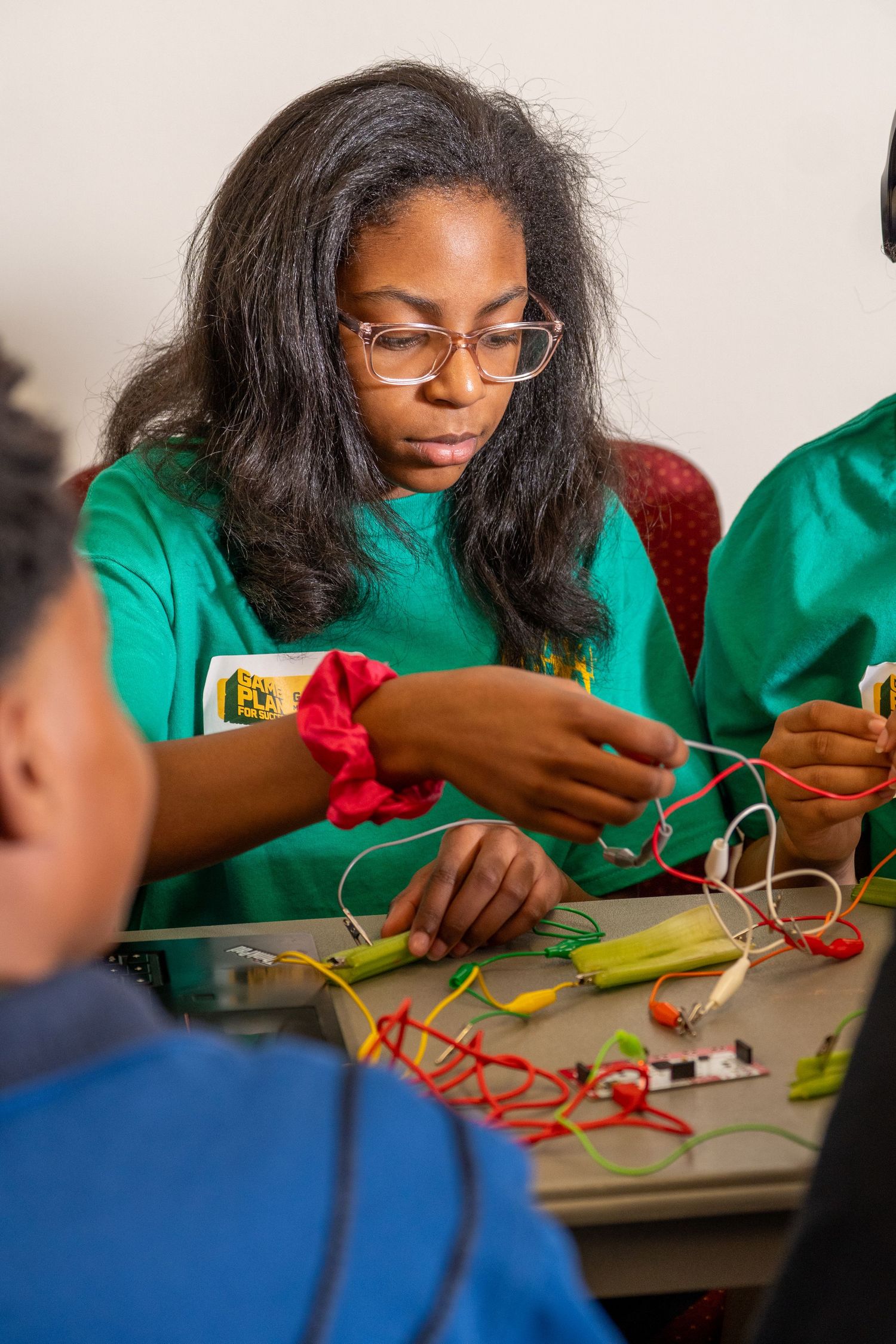 Young woman in green t-shirt works on electronics wiring project at a STEM education workshop.