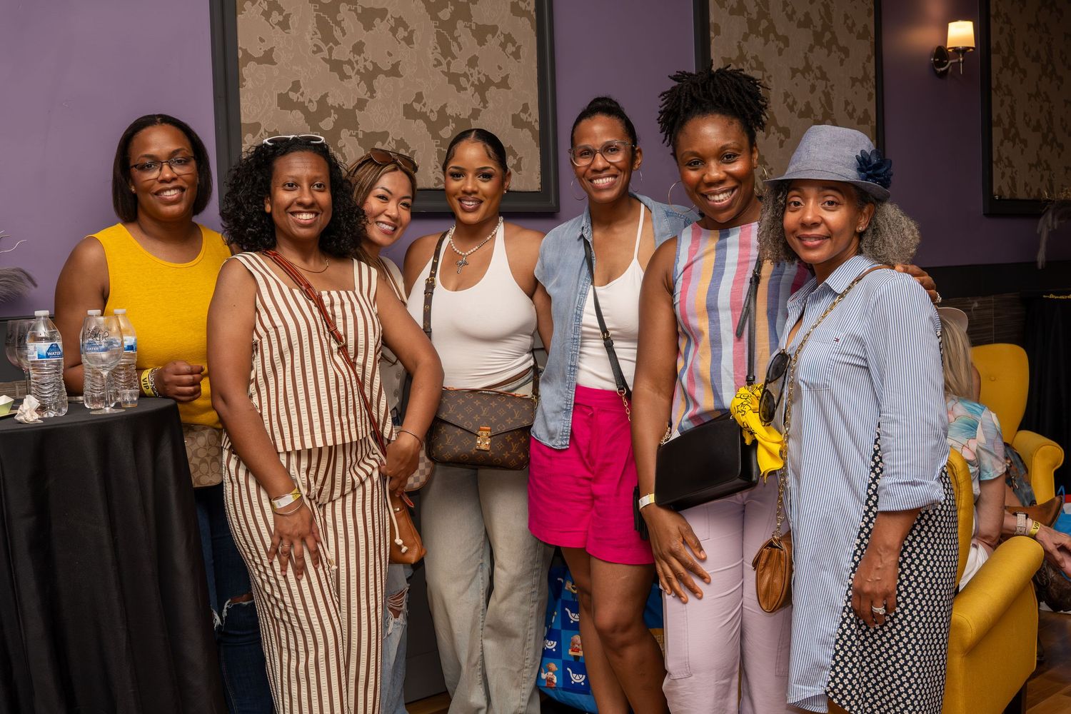 Group of seven women smiling together at an indoor social event.