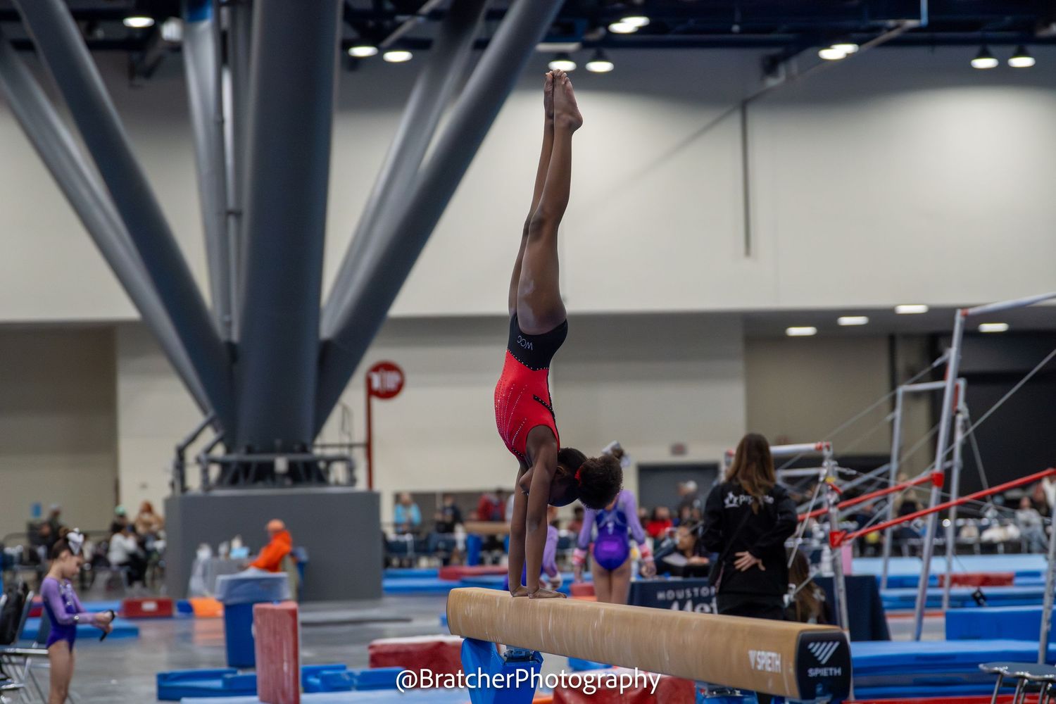 Skilled gymnast executes perfect handstand on balance beam at indoor gymnastics competition.
