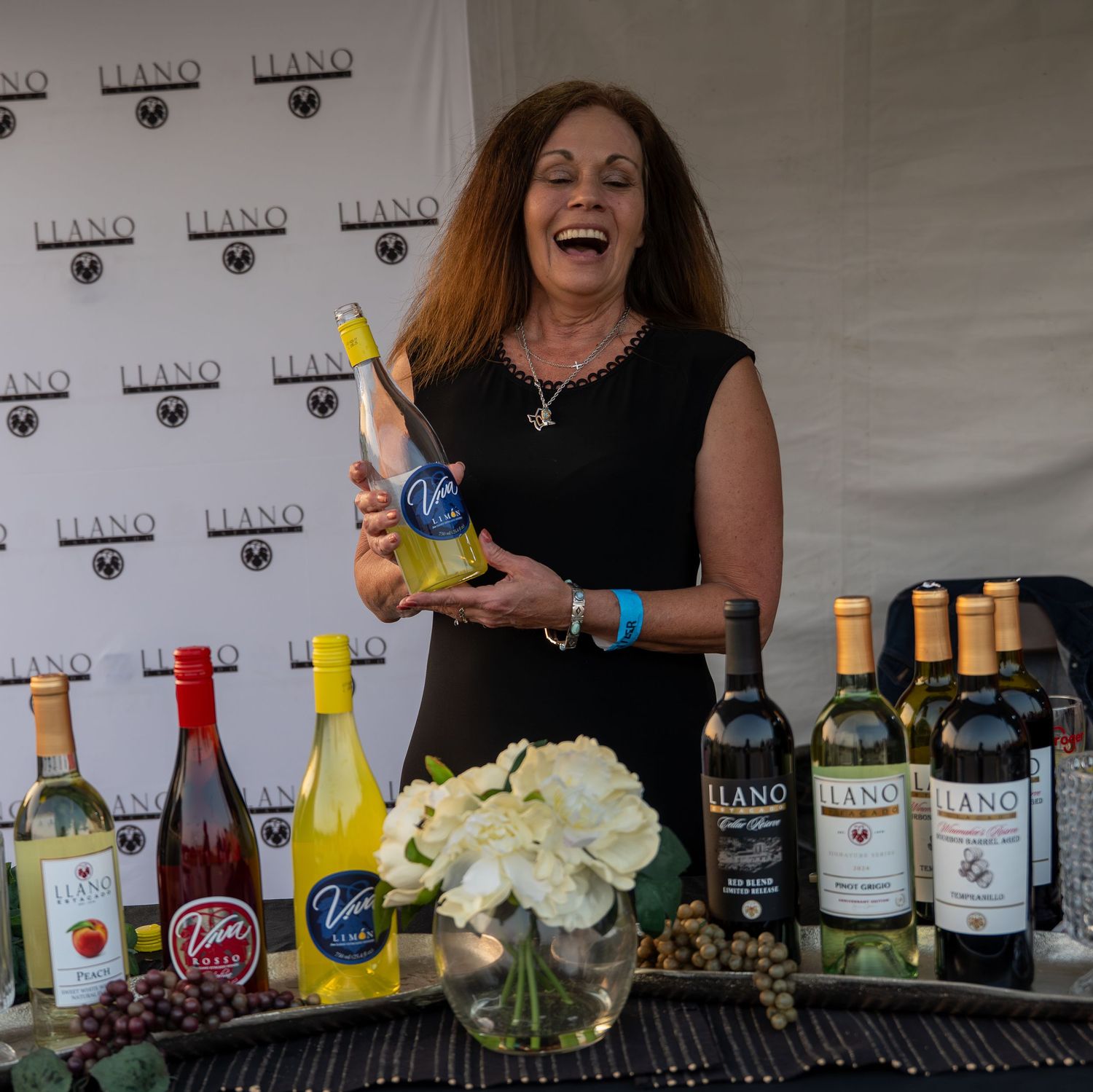Laughing woman holding up Llano wine bottle at a winery promotional tasting event.