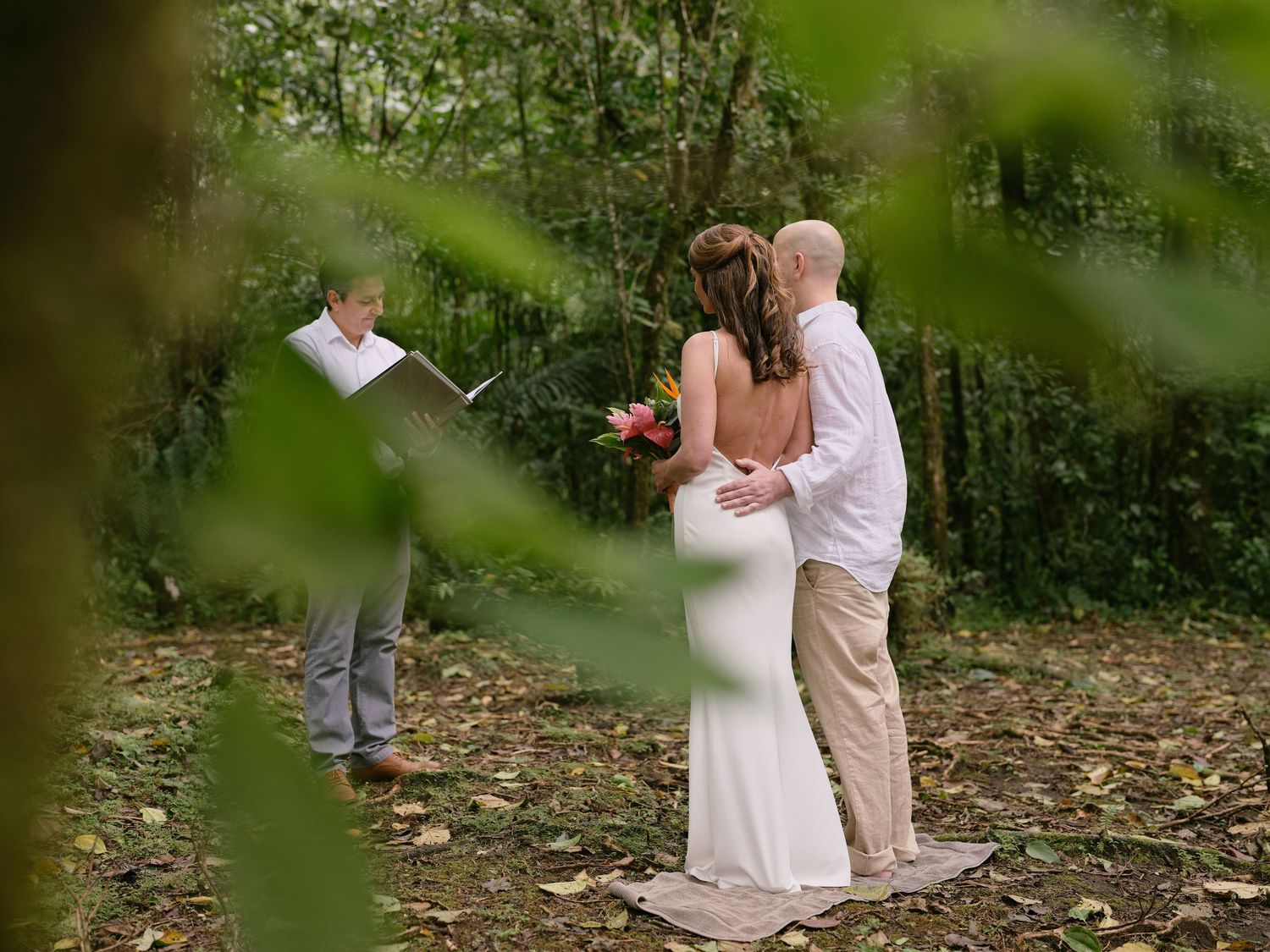 Intimate forest elopement ceremony with couple exchanging vows as officiant reads from a book outdoors.
