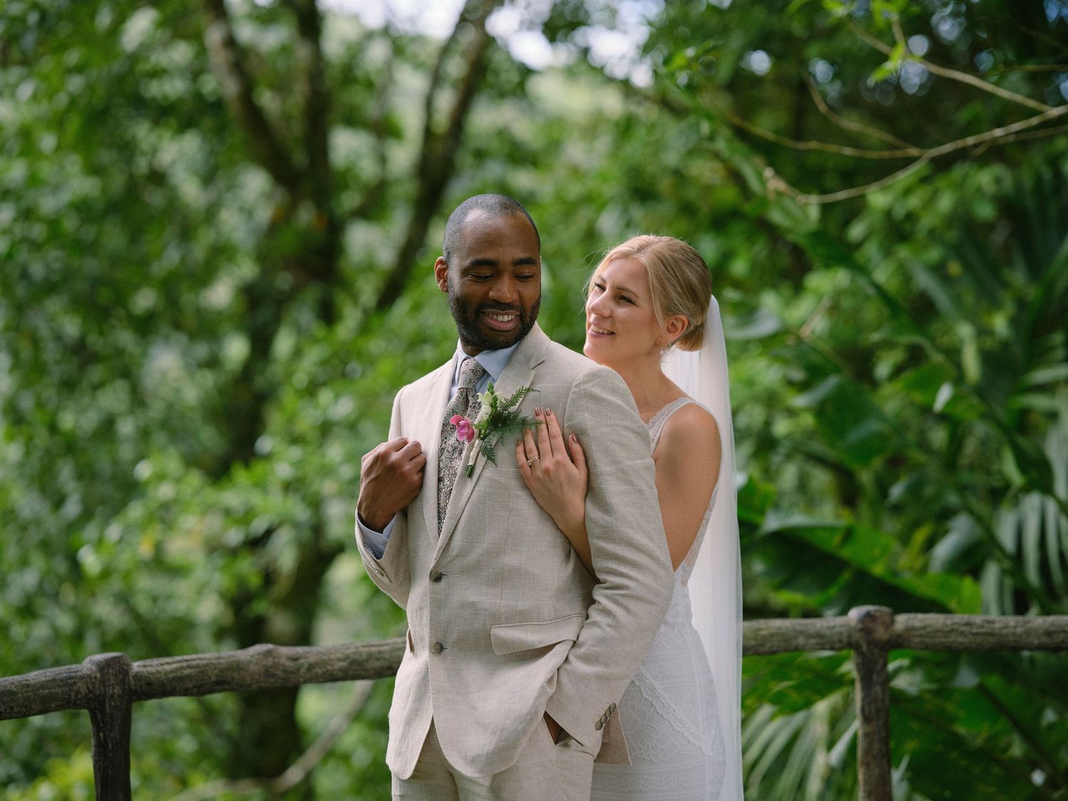 Smiling interracial wedding couple posing together in a verdant tropical garden setting.