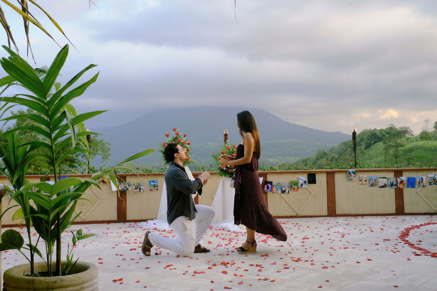 Romantic marriage proposal on a decorated terrace with rose petals and mountain volcano views at sunset.