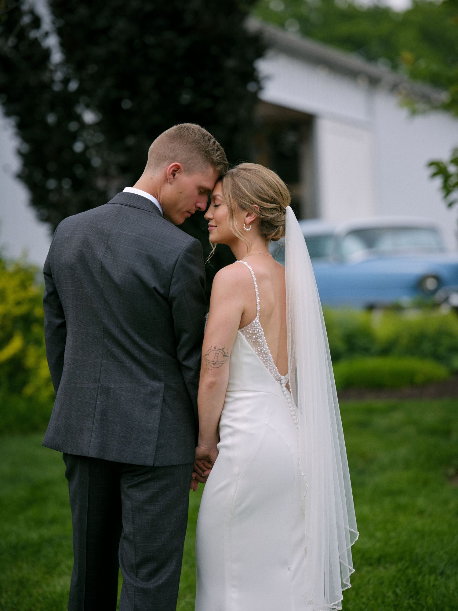 Bride and groom holding hands facing away showing intricate lace back wedding gown and flowing veil.