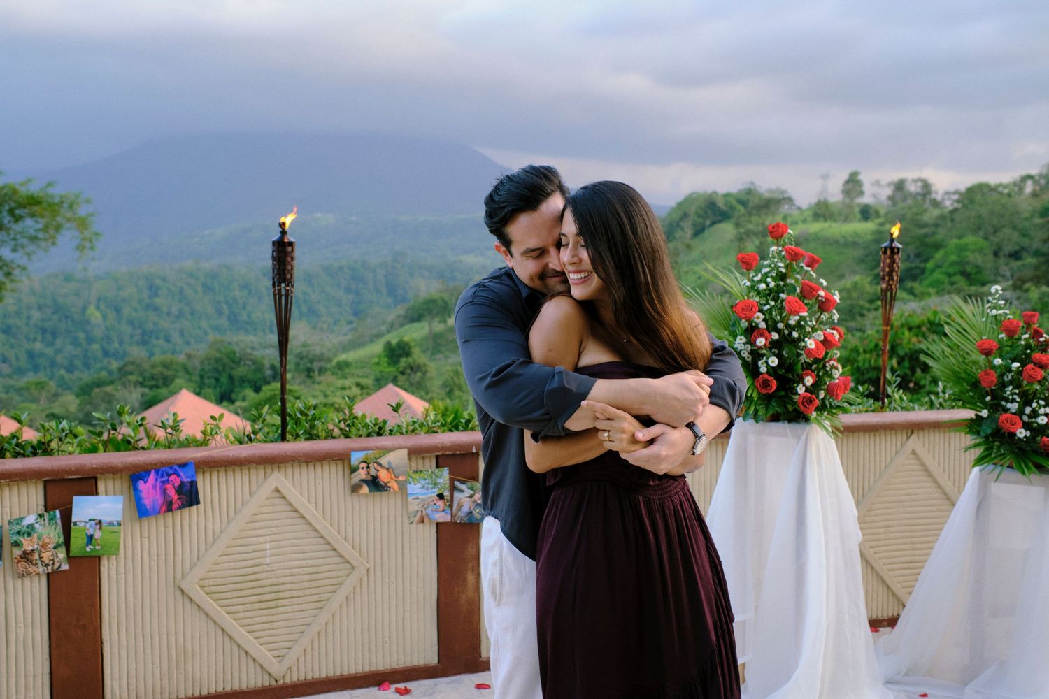 Couple sharing a joyful embrace on a flower-decorated terrace with stunning mountain landscape at sunset.