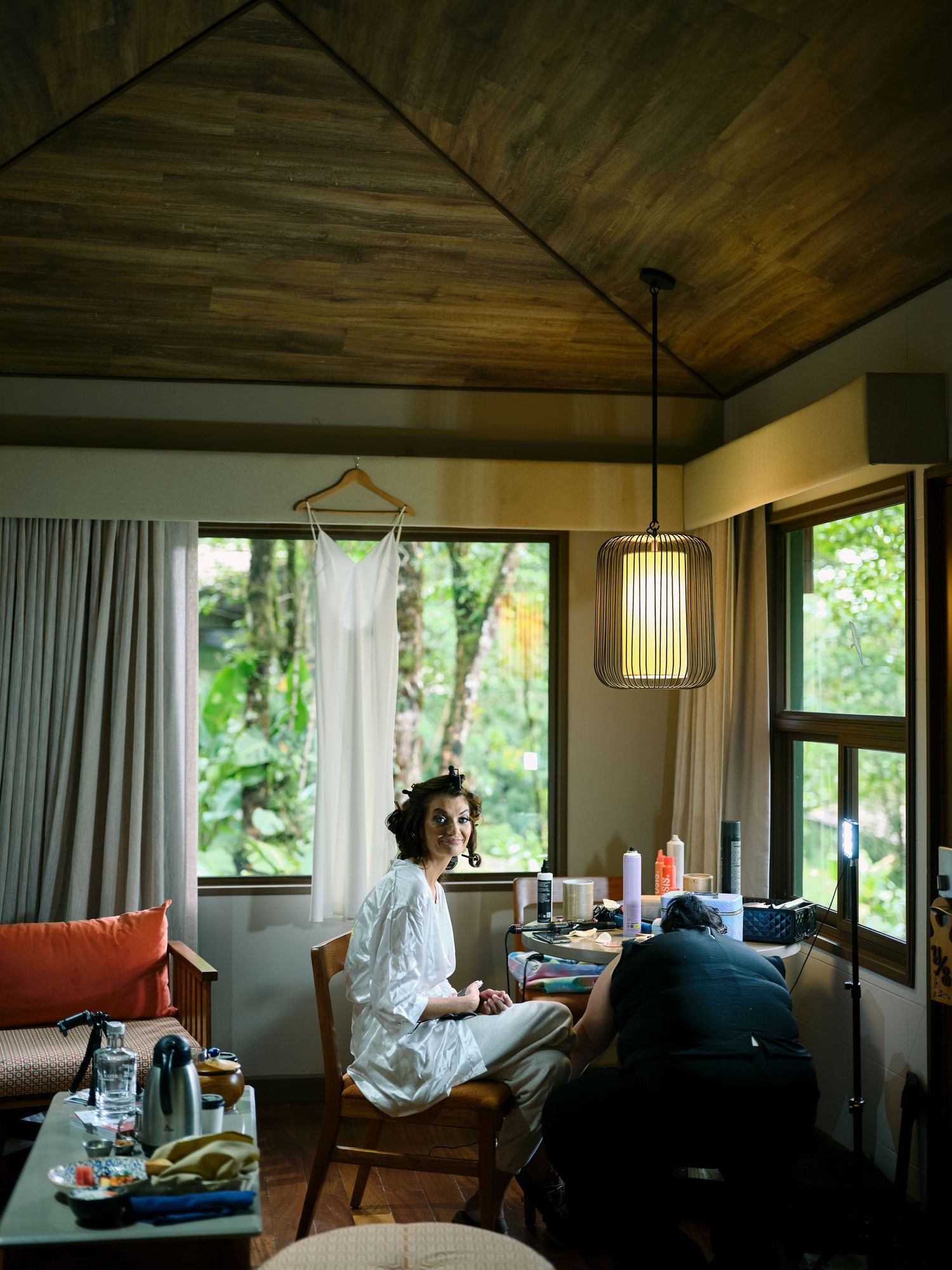 Bride getting ready in a beautifully lit jungle villa room with lush tropical greenery outside the windows.