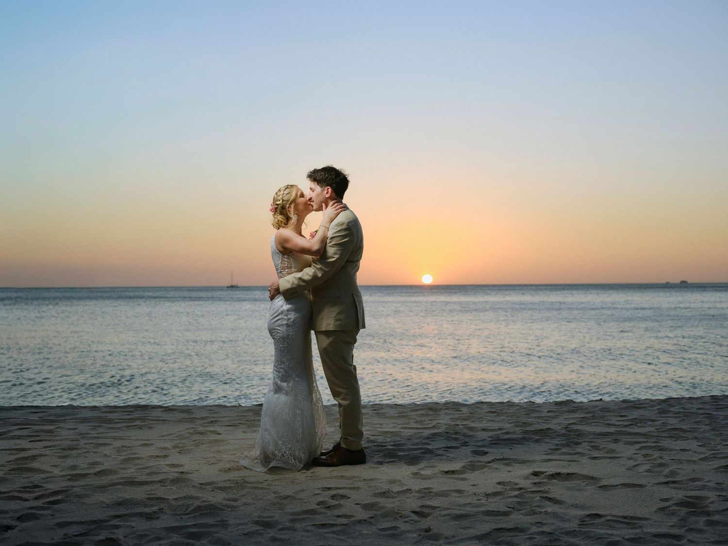 Bride and groom share a romantic kiss on the beach during a stunning sunset wedding.