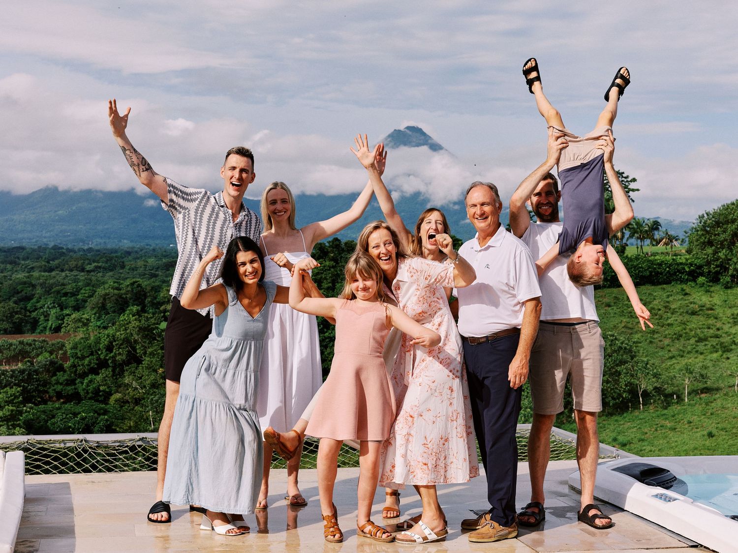 Joyful extended family celebrating outdoors on a terrace with a dramatic volcanic mountain view behind them.