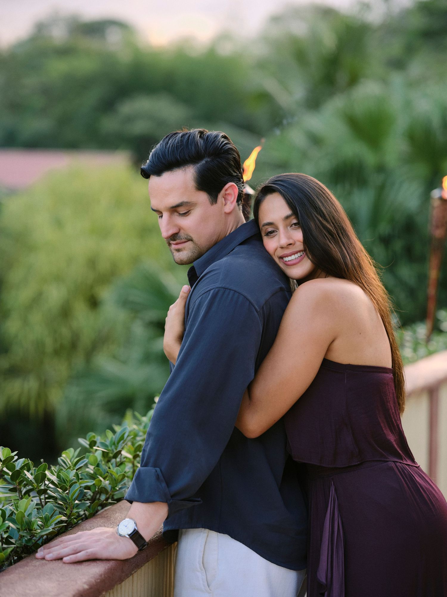 Romantic couple posing together on a balcony surrounded by tropical greenery at golden hour sunset.
