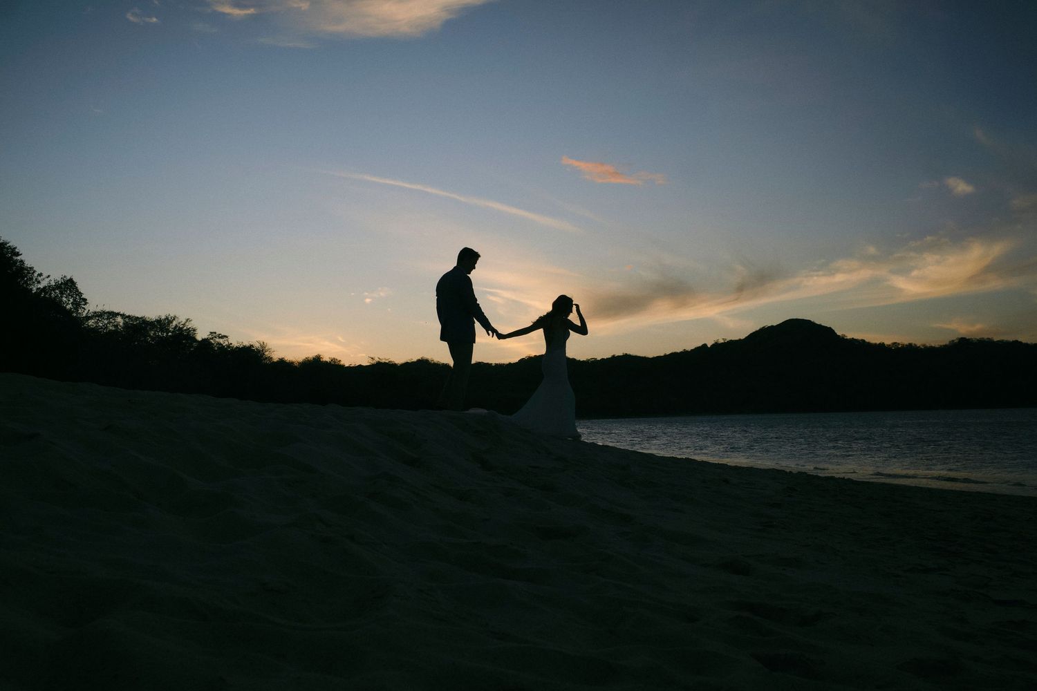 Silhouette of bride and groom holding hands on a beach during a breathtaking tropical sunset.