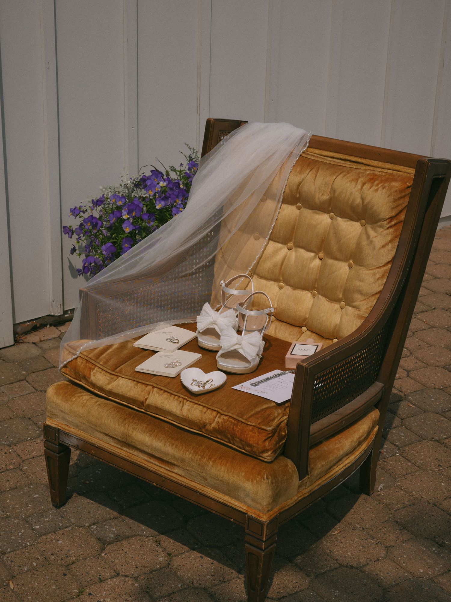 Elegant gold velvet chair displaying bridal accessories including white heels, veil, and wedding details.