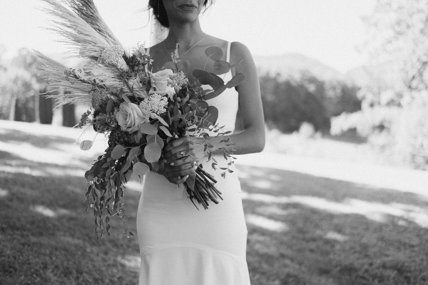Black and white photo of bride holding large boho floral bouquet outdoors.