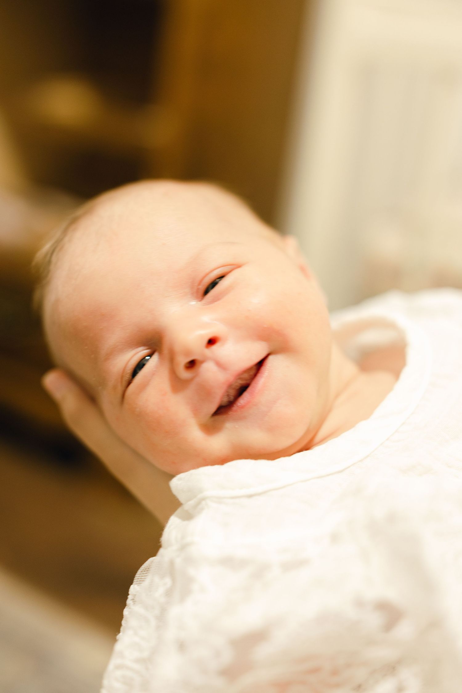 Smiling newborn baby in white outfit with eyes squinting in joy.