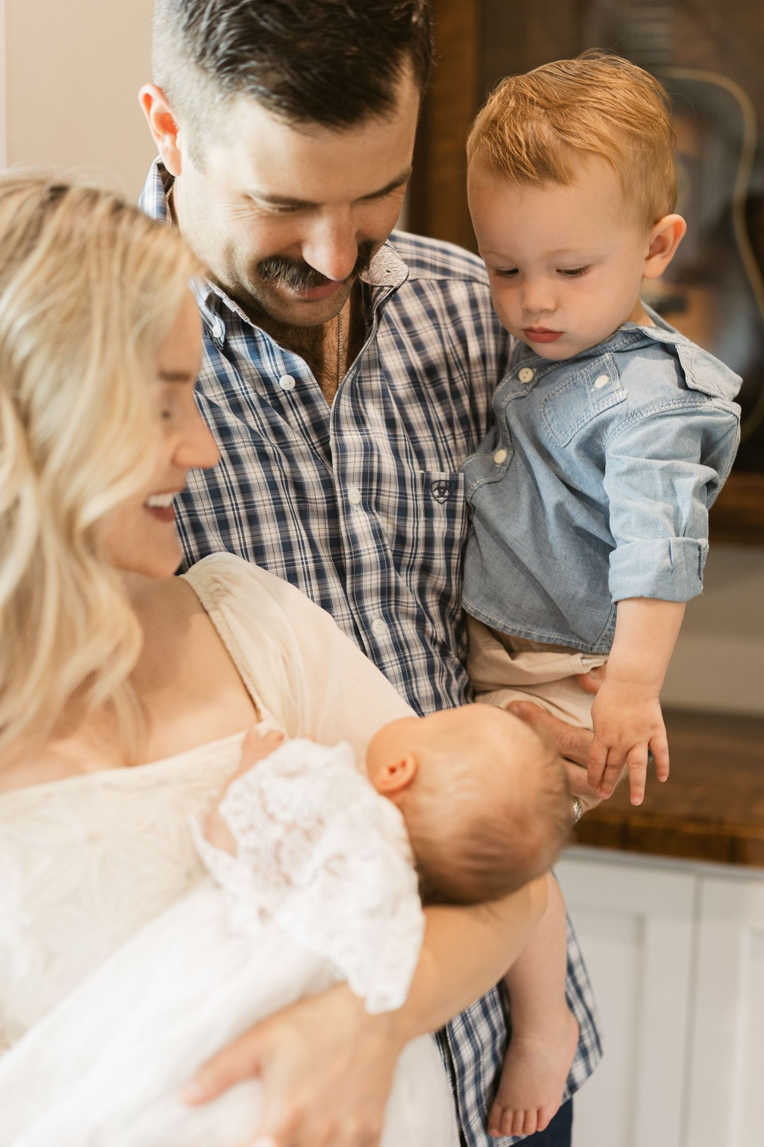 Happy family with parents holding newborn baby and toddler son smiling together indoors.
