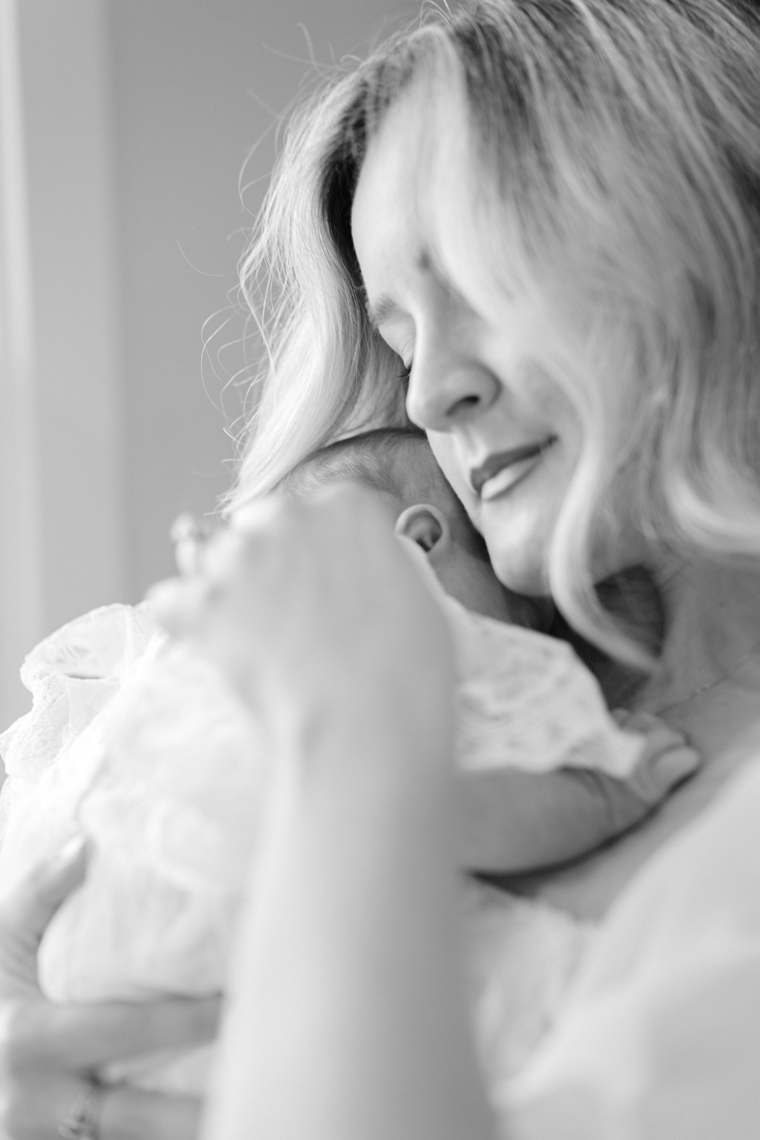Tender black and white portrait of a smiling mother gently holding her newborn baby close.