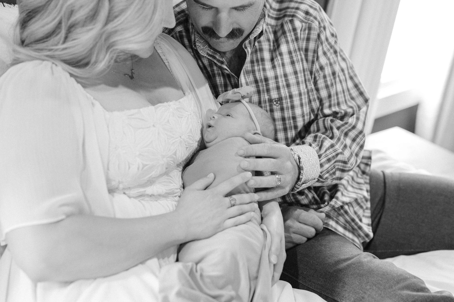 Black and white photo of new parents lovingly gazing at their newborn baby during an intimate family portrait session.