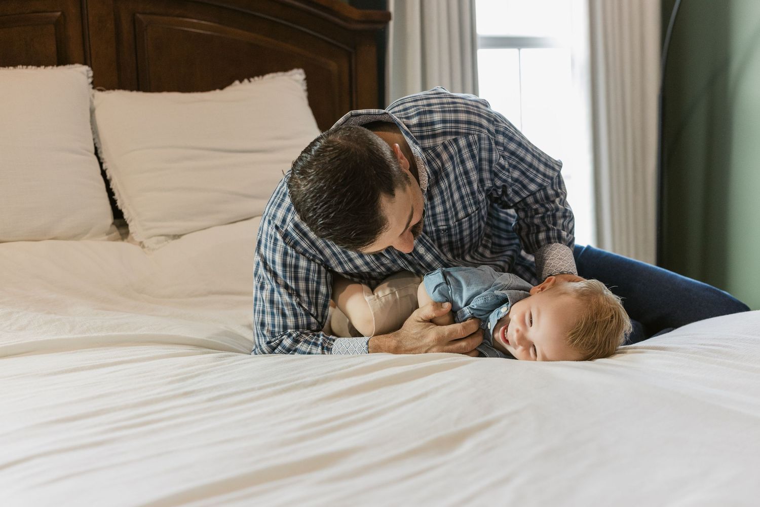 Father leaning over newborn baby lying on white bed, sharing a tender bonding moment.
