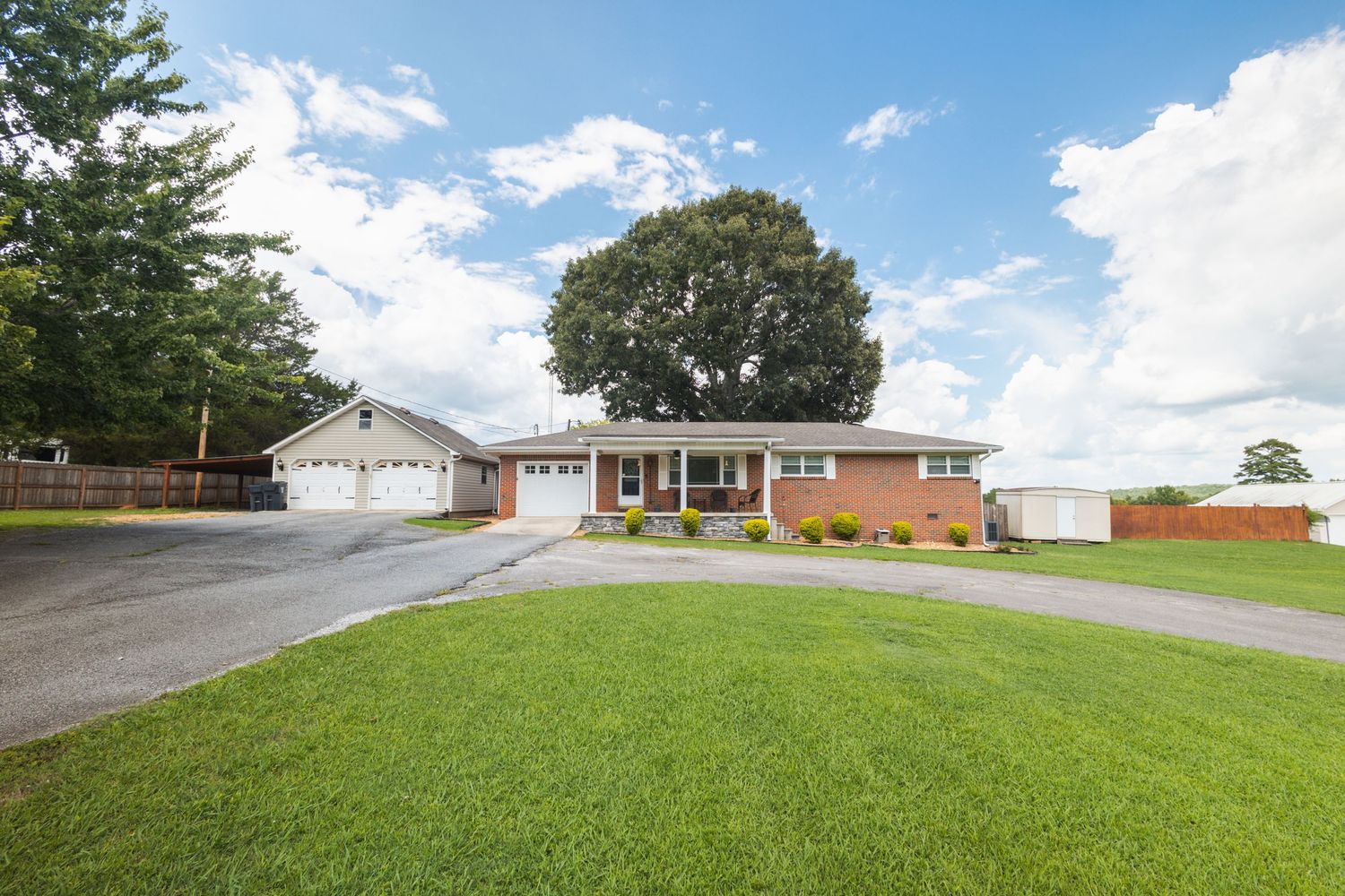 Brick ranch home with attached garage, large shade tree, and well-maintained green front lawn.